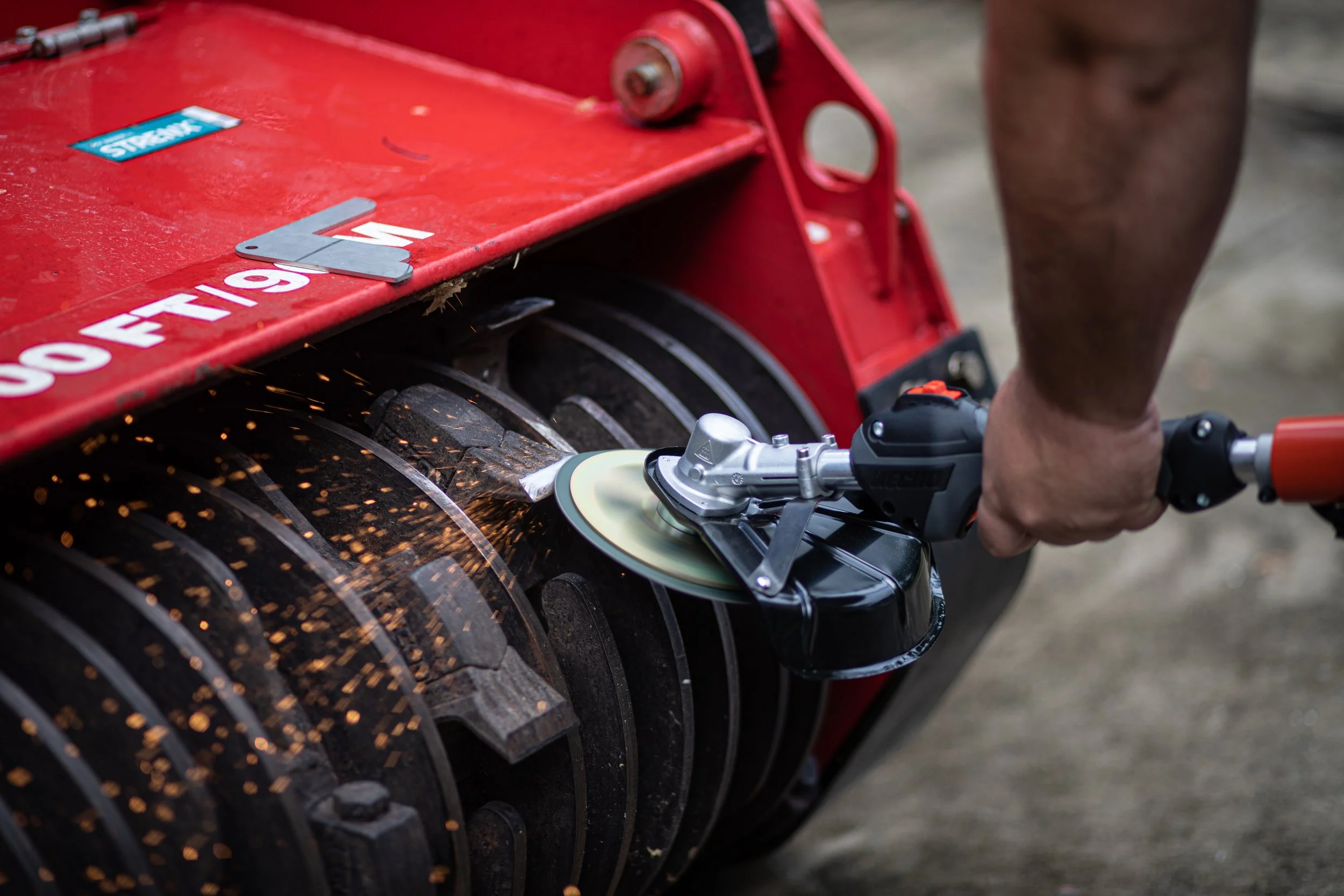 Close-up of a person using a power sander on a large tire, with sparks flying from the sanding process.