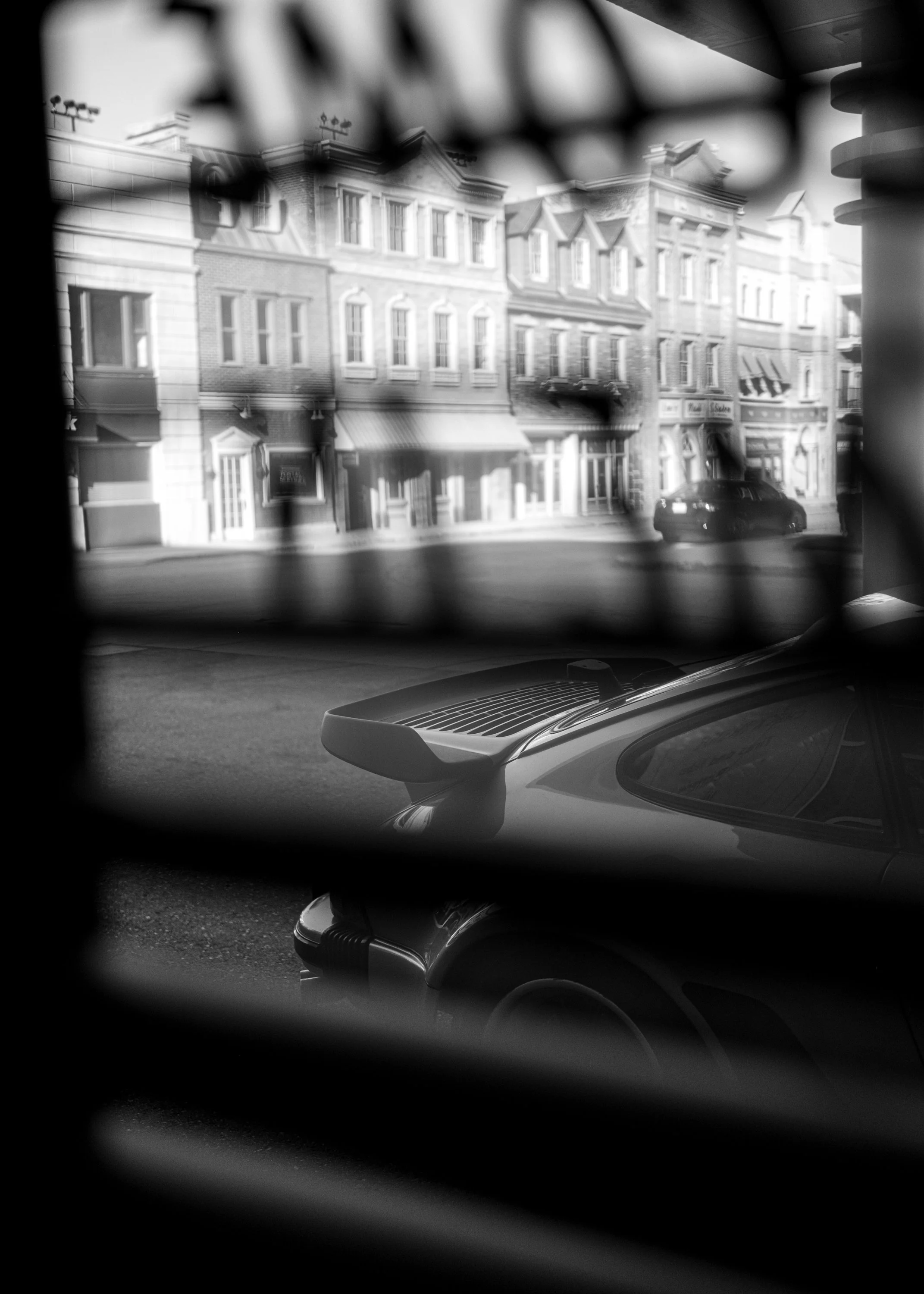 View of a row of historic buildings across the street, seen through a partially obscured window with a black frame and decorative elements.
