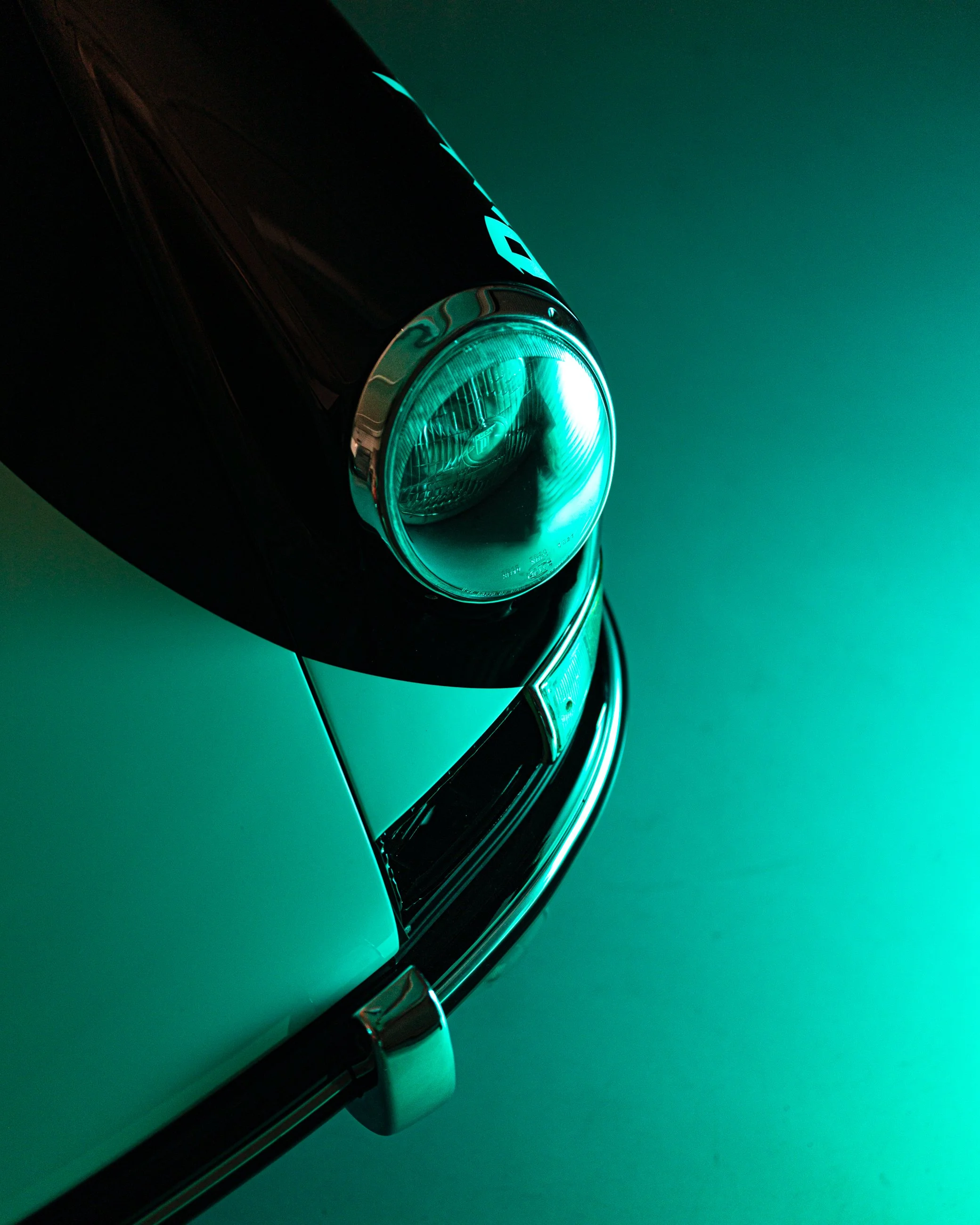 Close-up of a car headlight with a glow in teal color, against a solid teal background. Porsche 911.