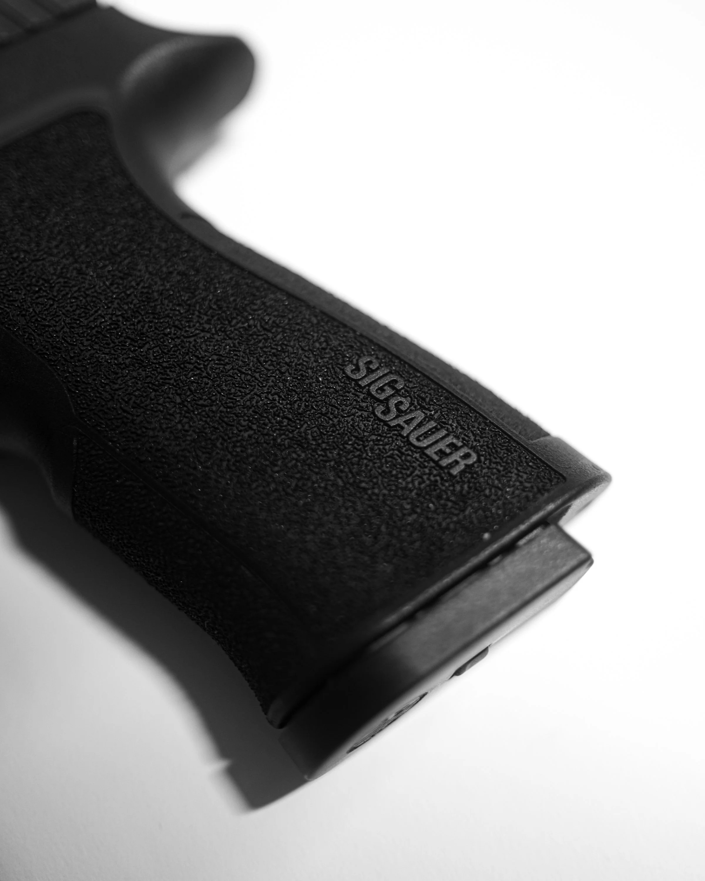Close-up of a black textured grip on a camera, with partially visible text that reads Sig Sauer. Sig Sauer.