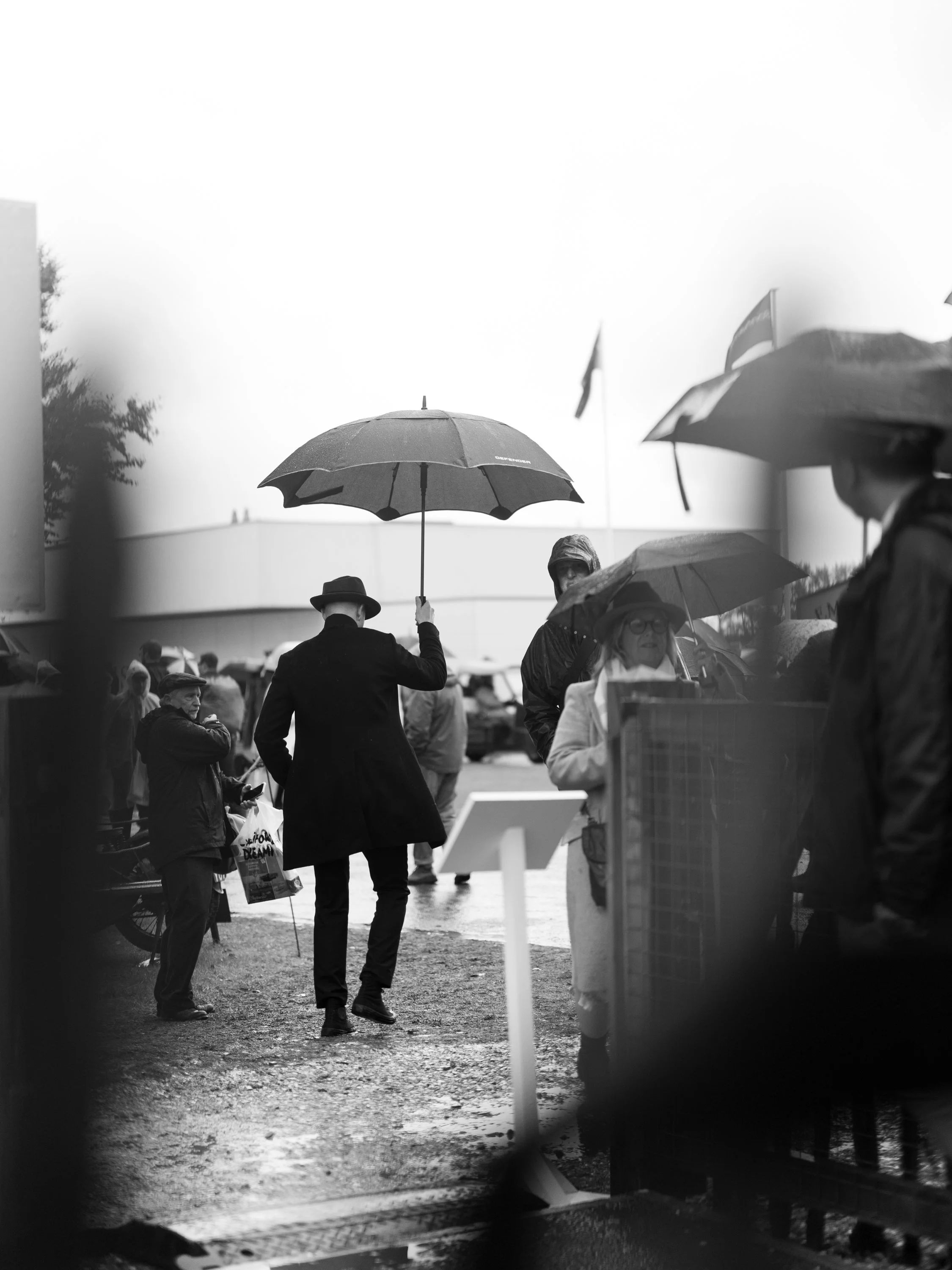 People holding umbrellas in a crowd during rainy weather, seen through a glass window.