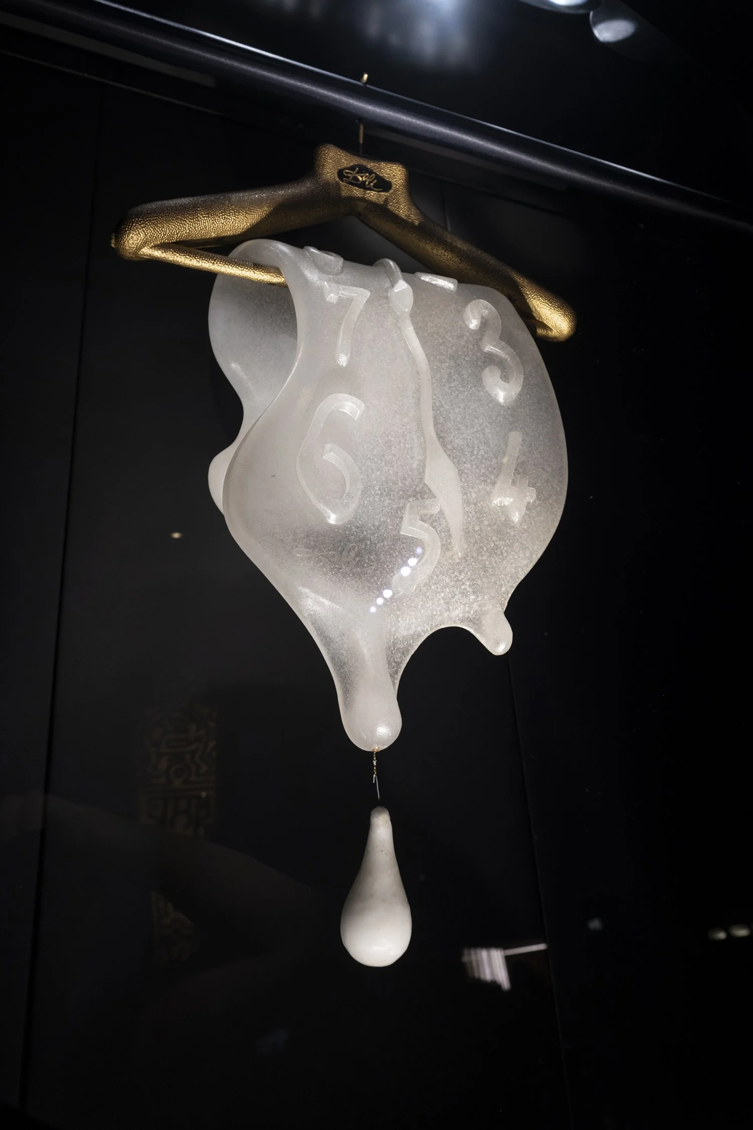 An art installation resembling melting clocks in a surrealist style, with one clock appearing in a translucent, irregular shape and the other in a gold-like textured frame, hanging against a dark background. Swarovski.