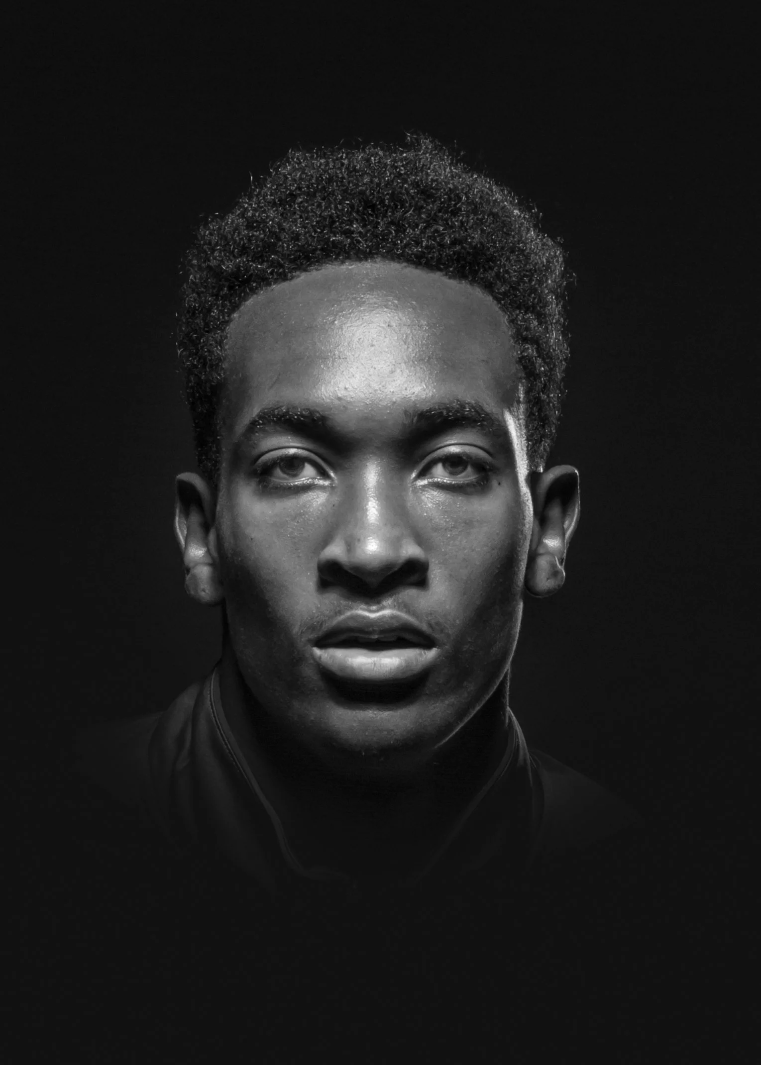 Black and white portrait of a man with natural hair, looking directly at the camera against a dark background.