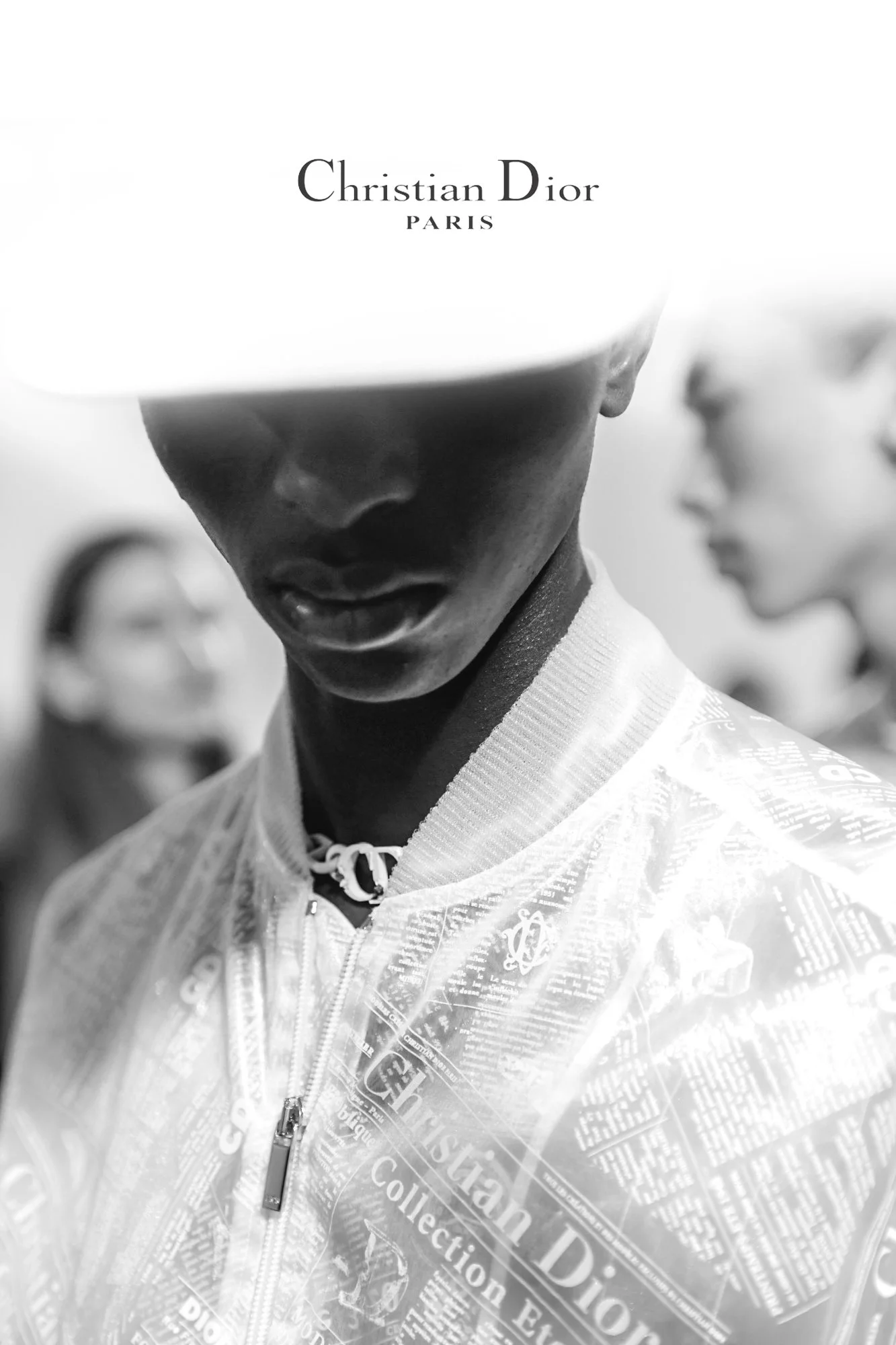 Close-up black-and-white photograph of a young male athlete in a sports jacket, with people blurred in the background, and the logo of Christian Dior Paris overlaid at the top. Christian Dior.