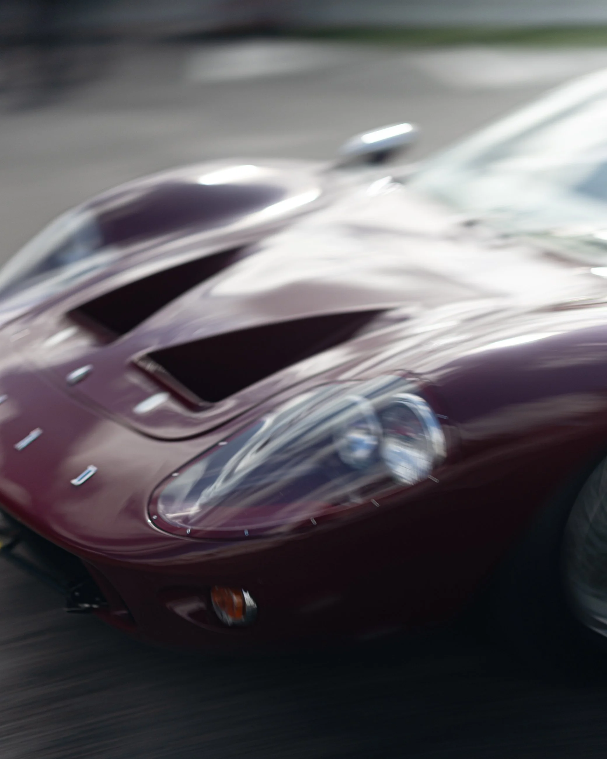 Close-up of a shiny red sports car with sleek lines, headlight, and front grille visible, speeding on a road.