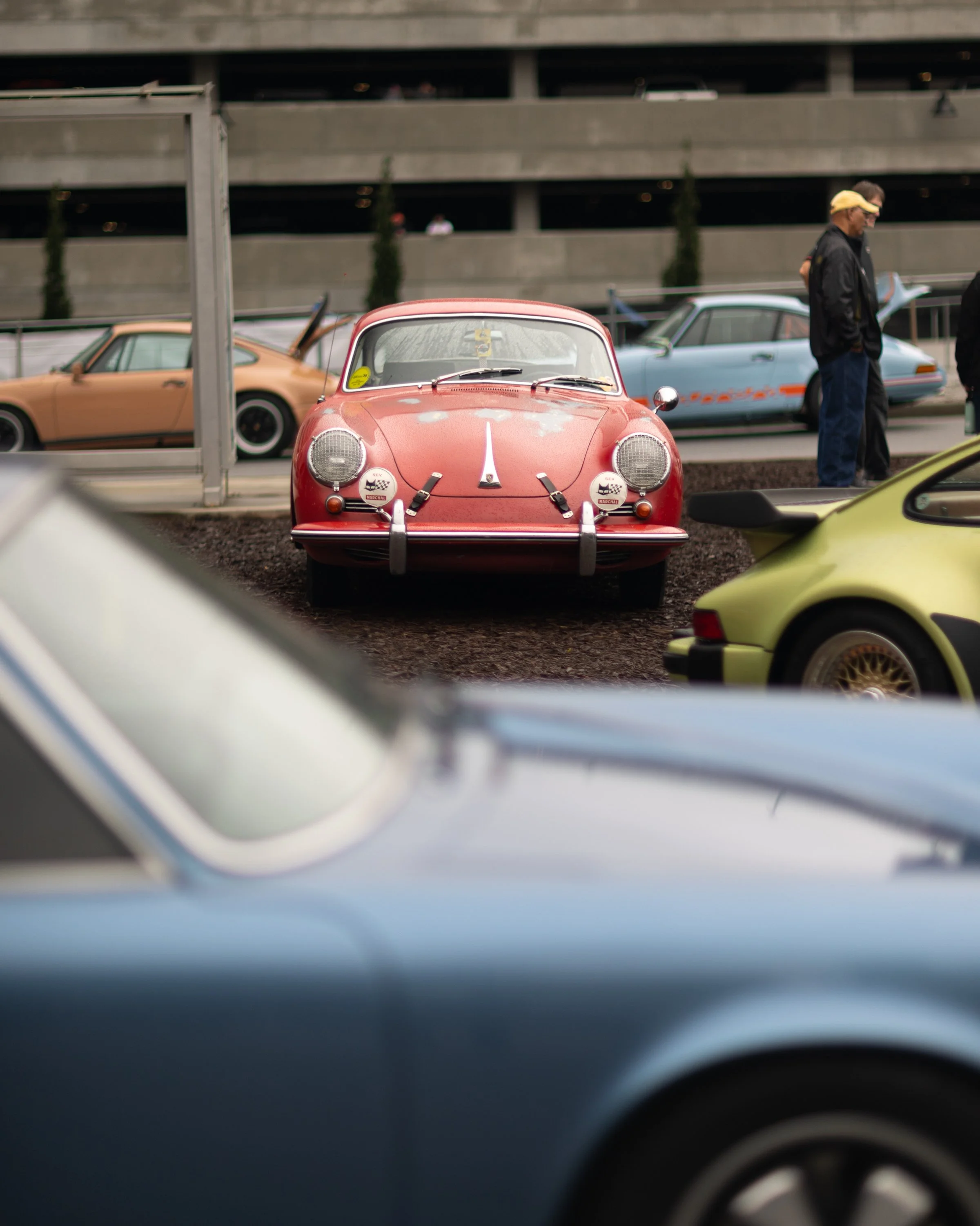 Classic red vintage sports car displayed among other classic cars, with a man standing beside it.