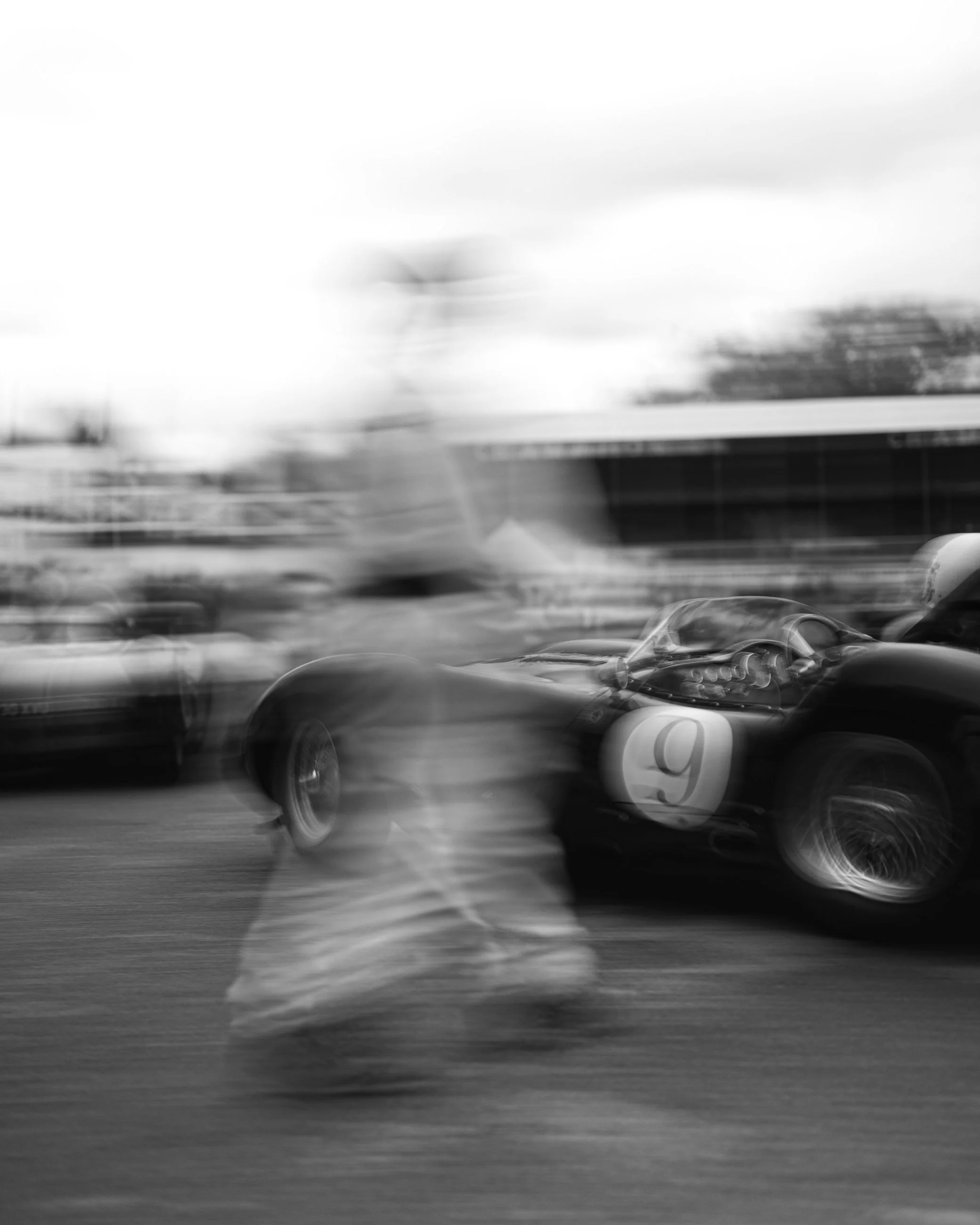 Blurry black and white image of multiple cars driving at high speed on a road. Goodwood Revival. Goodwood Revival