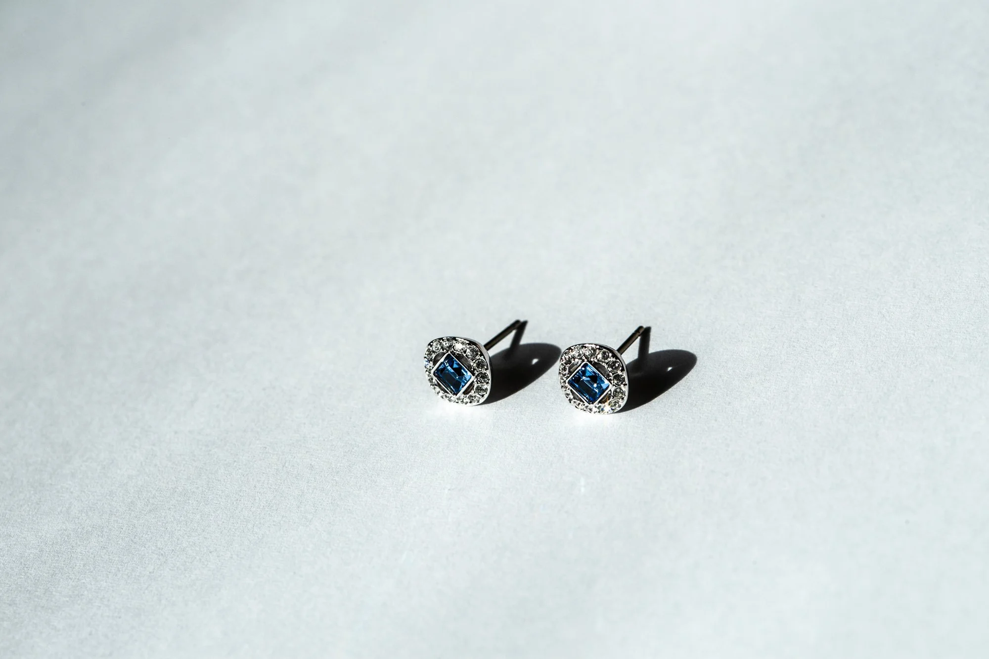 Pair of silver earrings with blue gemstones and surrounding clear stones on a light gray background.