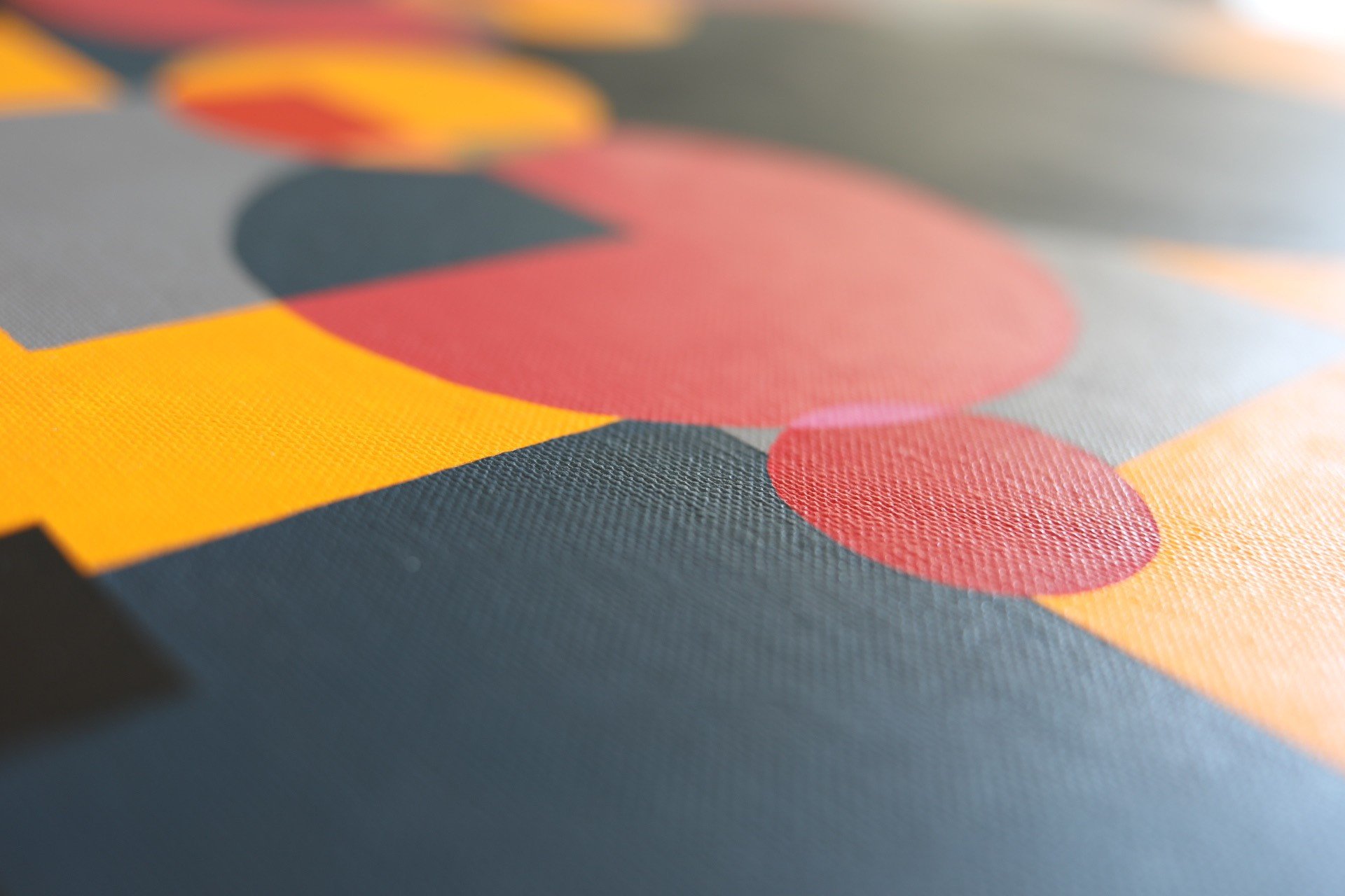 Close-up of a printed fabric with a pattern of overlapping circles in red, orange, and yellow on a gray background.