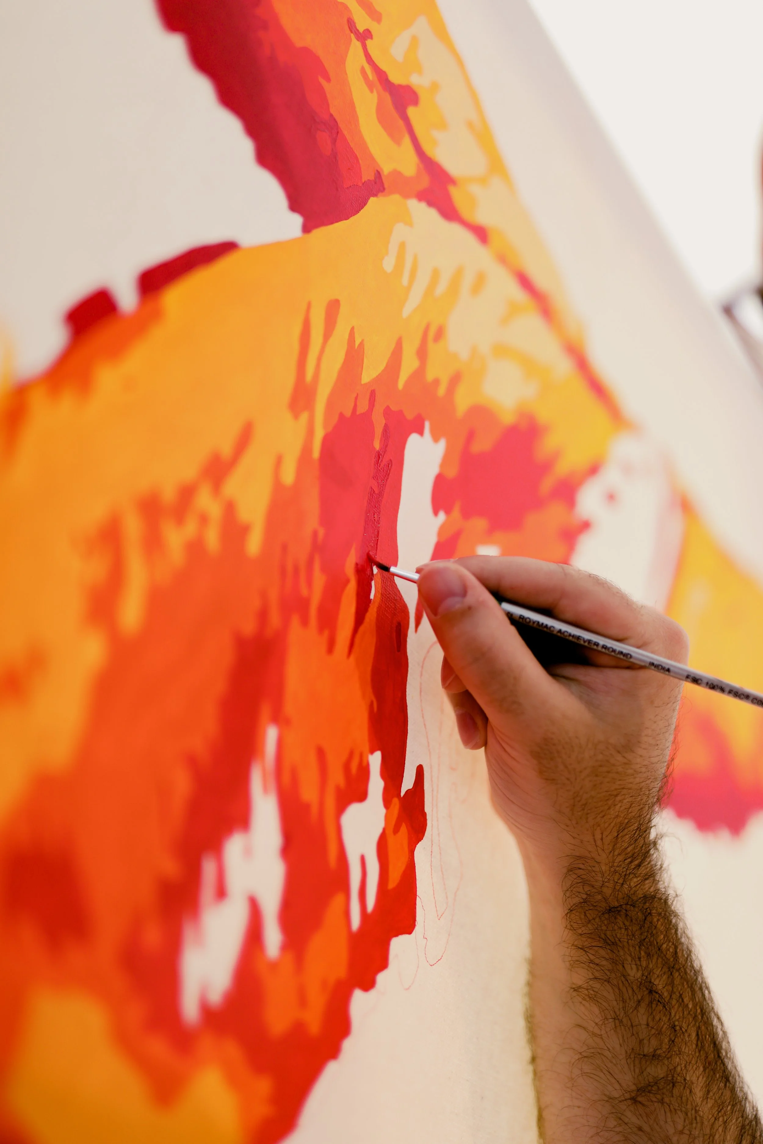 A person painting a colorful map on a large wall, using a fine brush, with visible arm and hand holding the brush.