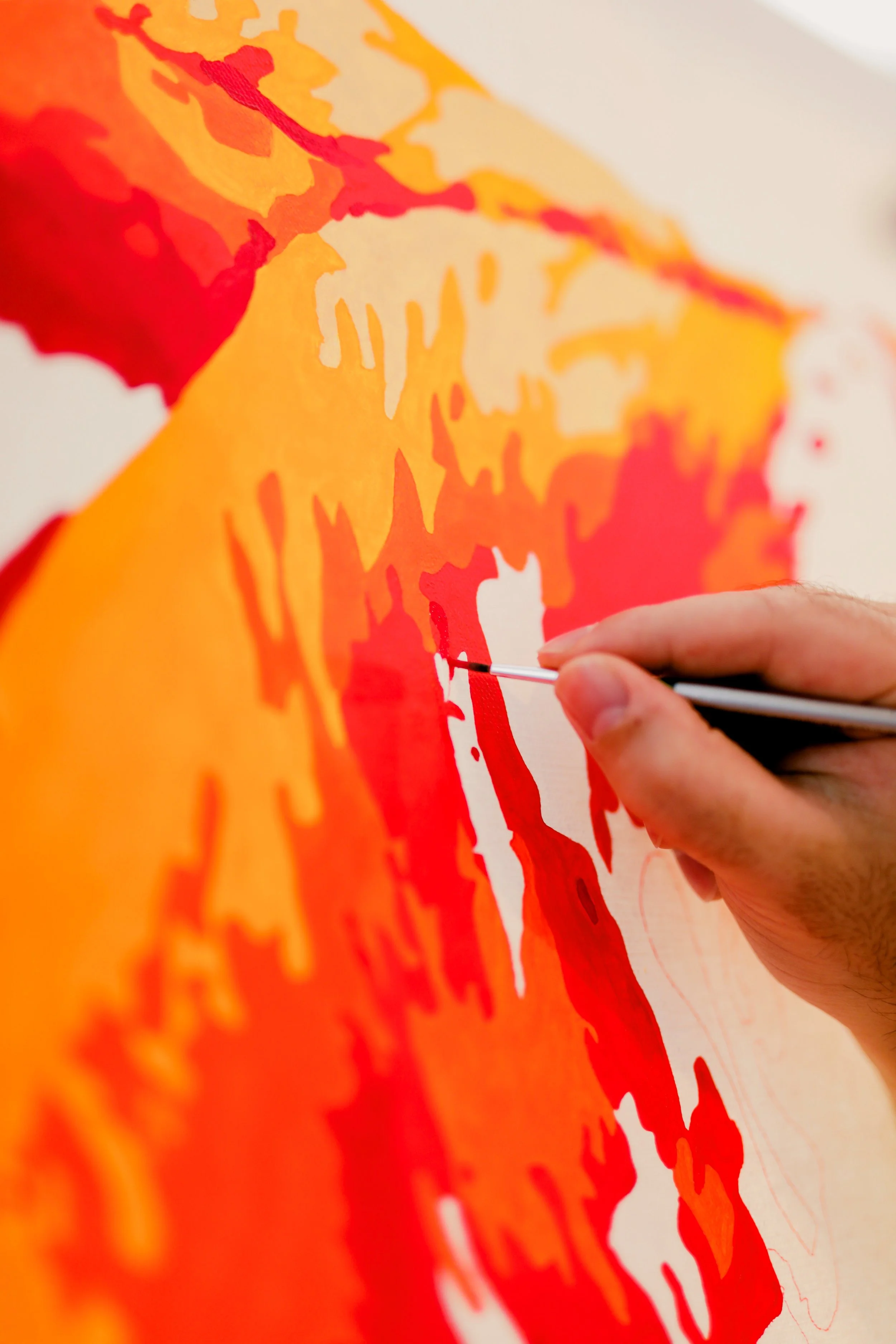 Close-up of an artist's hand painting a colorful map using a fine brush on a large canvas.
