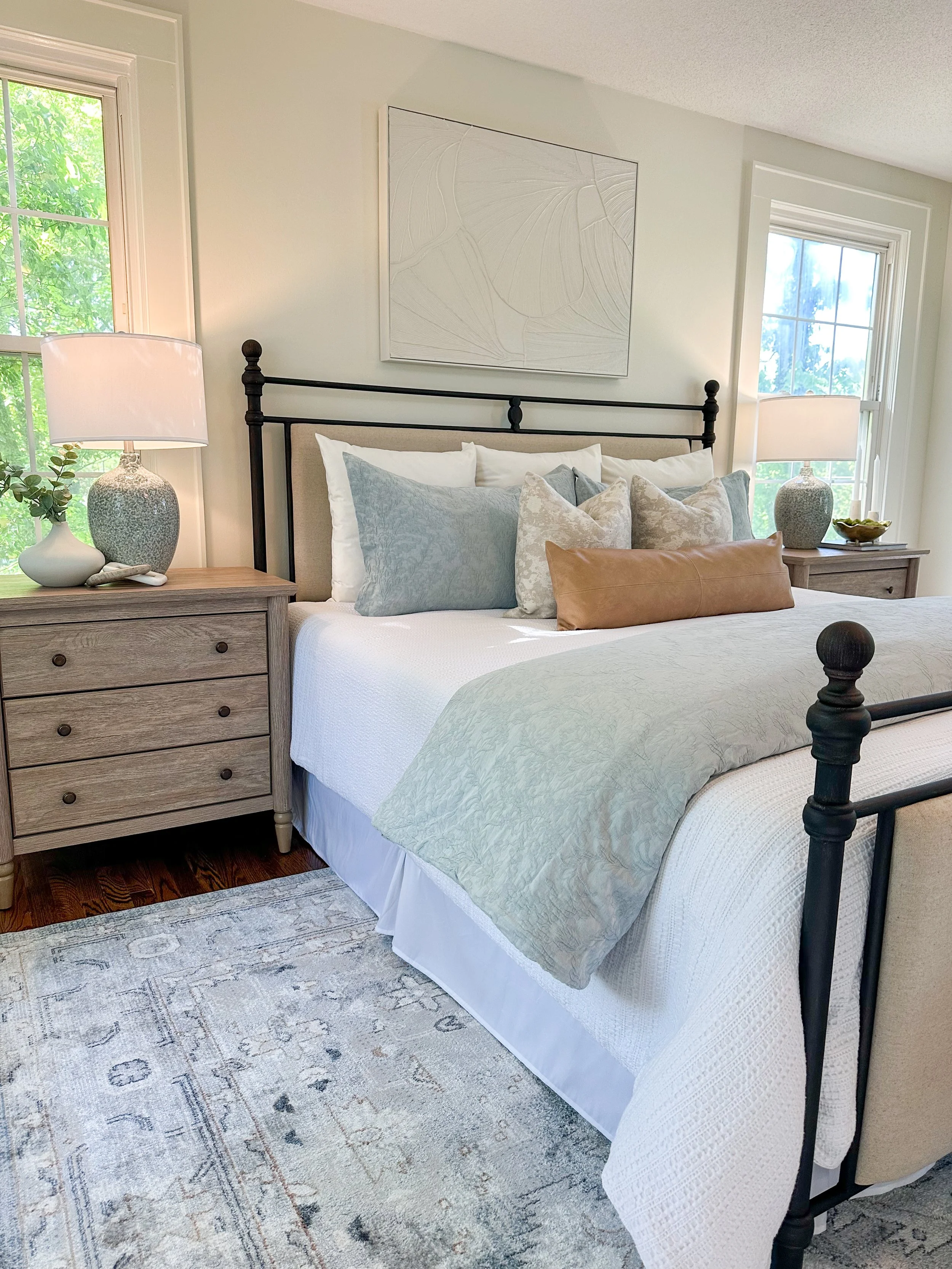 A bedroom with a bed, nightstands, lamps, and a window with green trees outside.