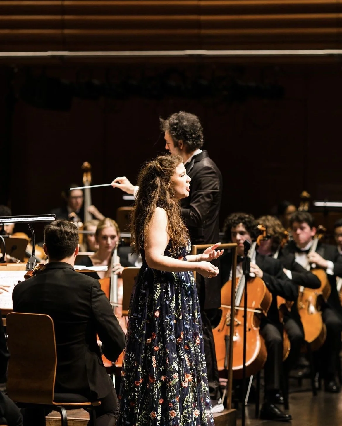 A female singer performing on stage with an orchestra behind her.