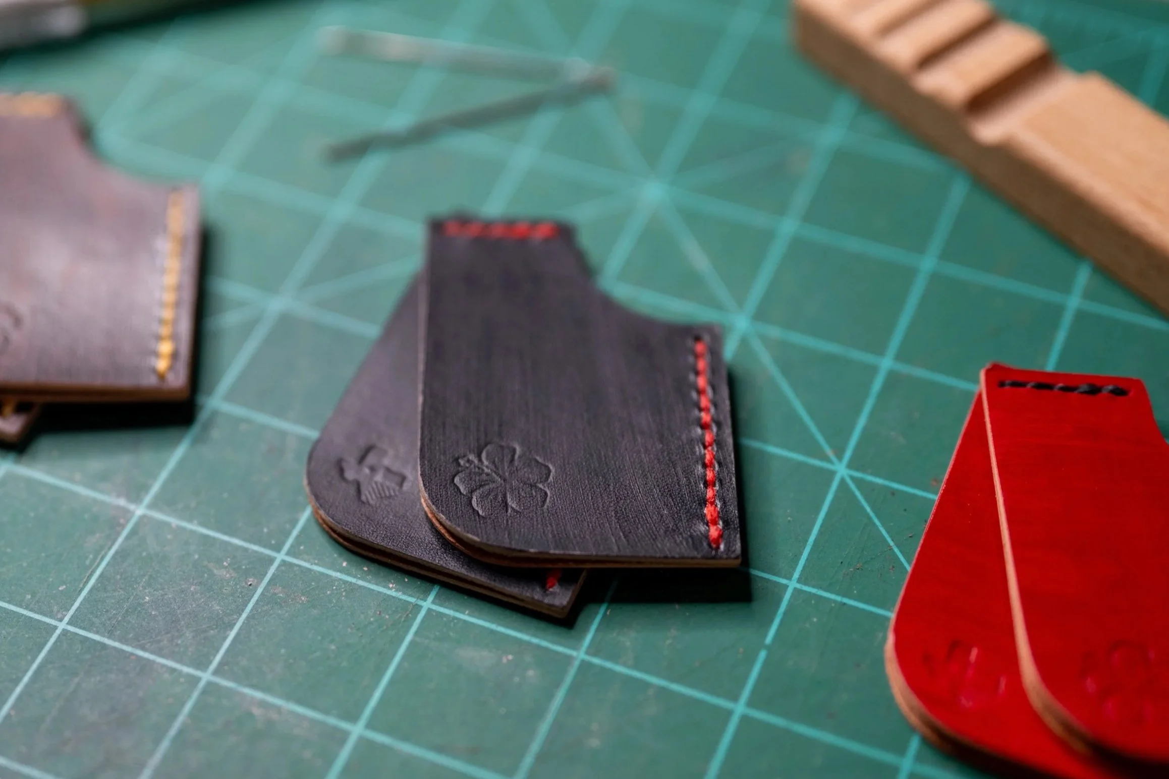 Close-up of black, gray, and red leather pieces with embroidery on a green cutting mat with grid lines.