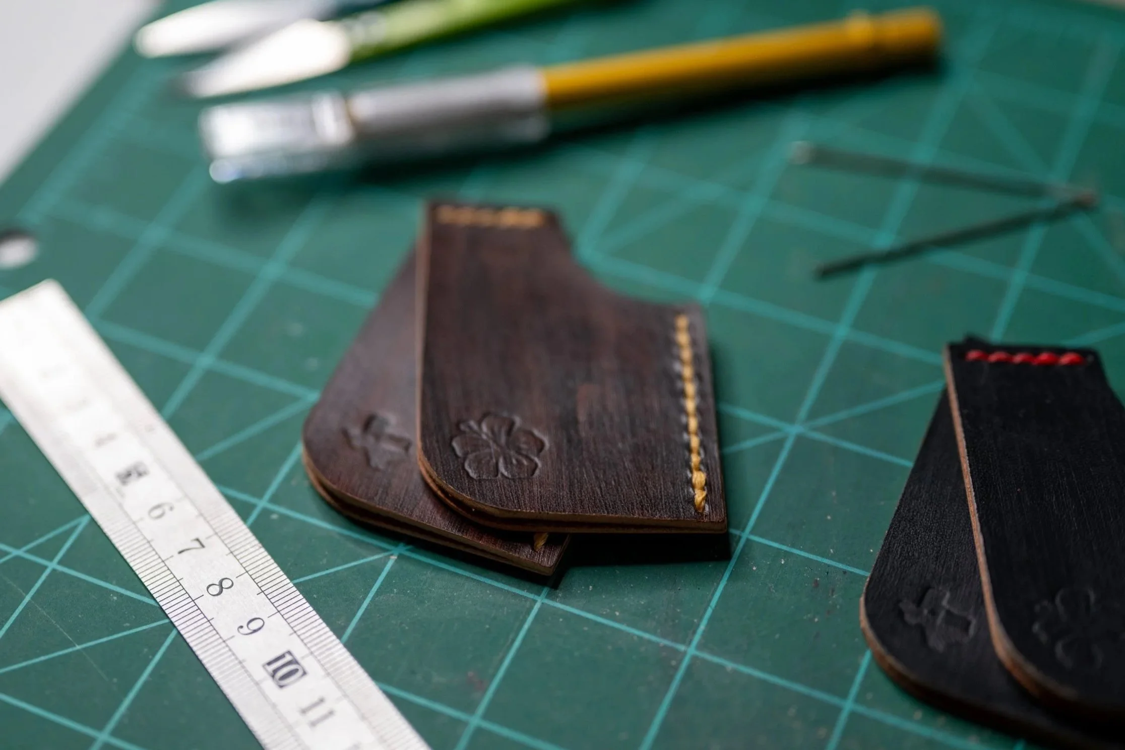 Close-up of leather keychains with embossed flower designs, placed on a green cutting mat with measurement ruler and crafting tools in the background.