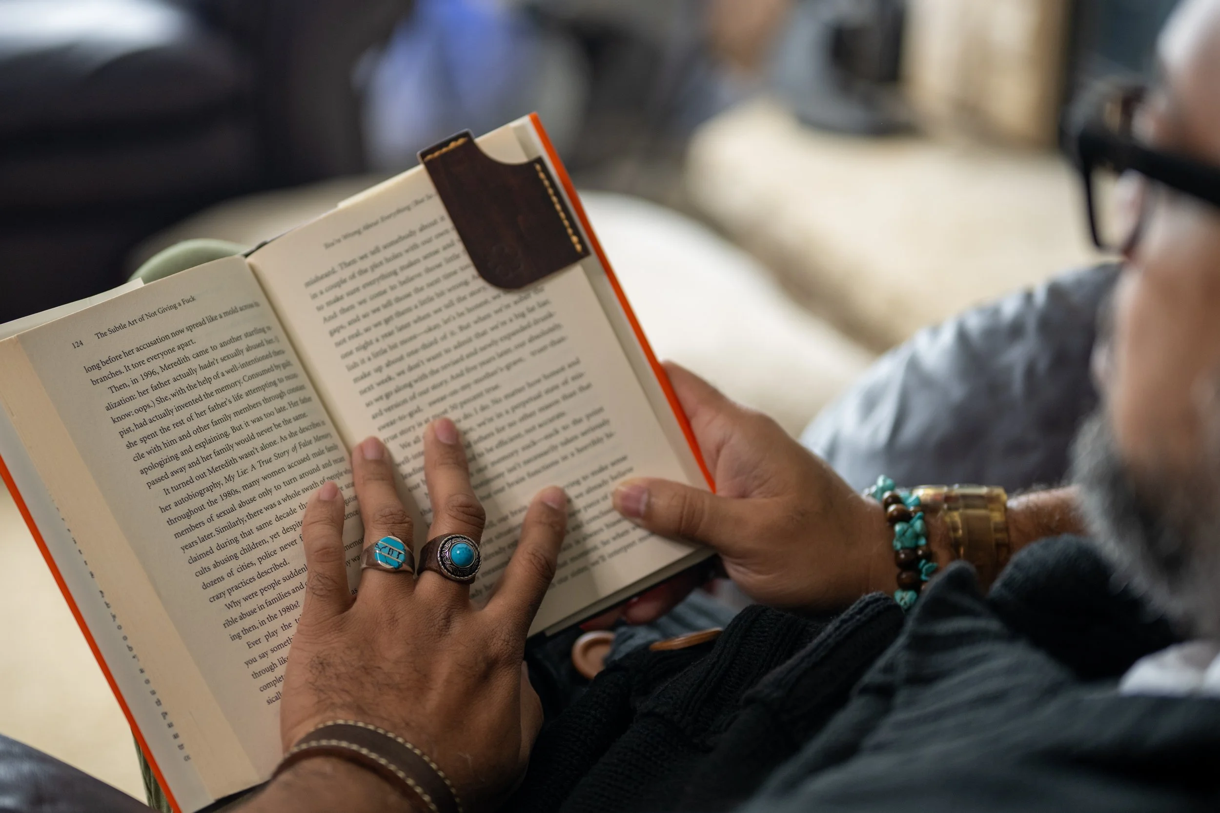 Person reading a book with a bookmark, wearing multiple rings and bracelets.
