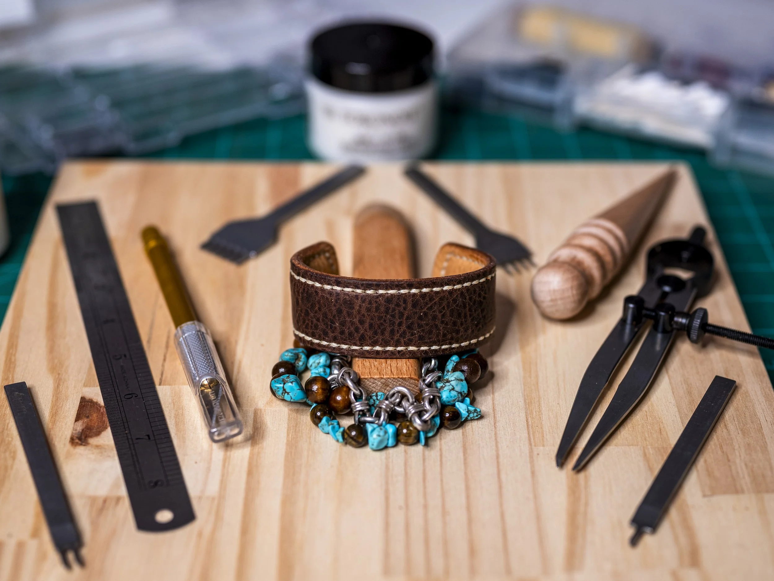 Tools and accessories for leatherworking, including a leather bracelet, beads, a watch, and various leatherworking tools on a wooden workbench.