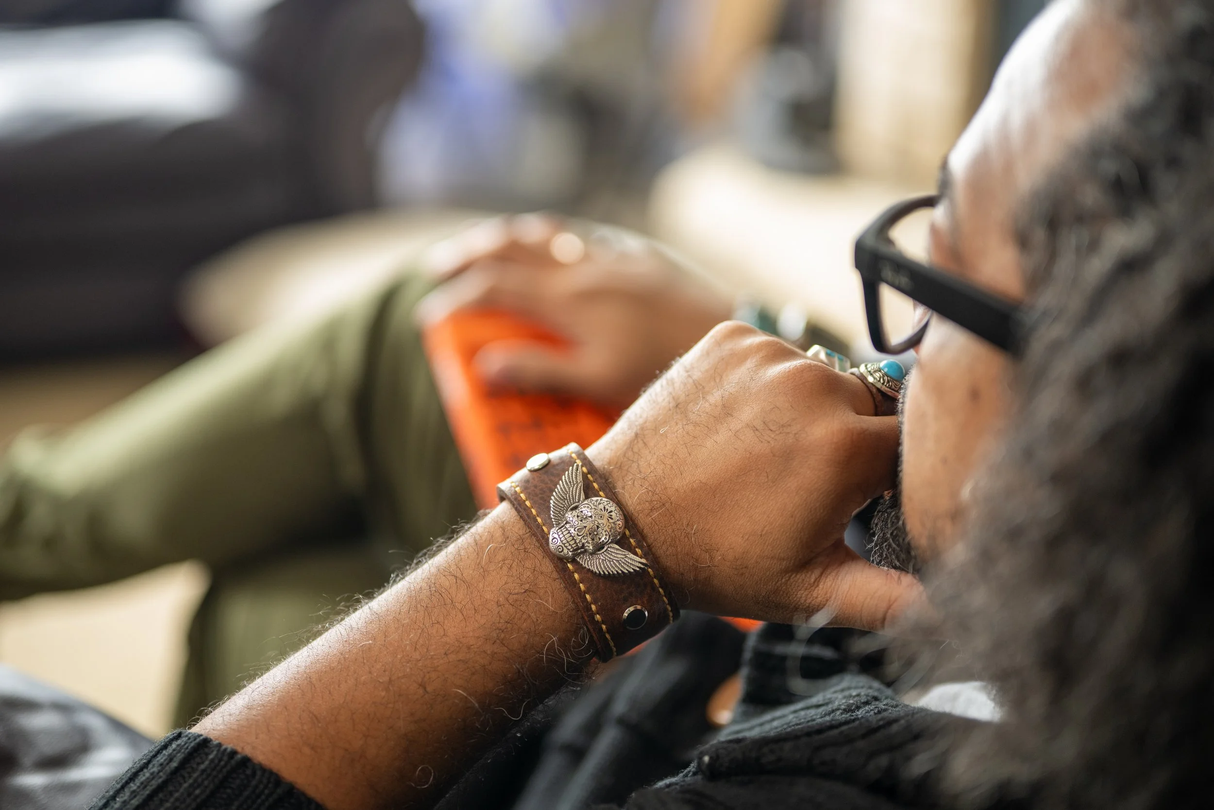 A person wearing glasses and jewelry, resting their head on their hand, with a blurry background.