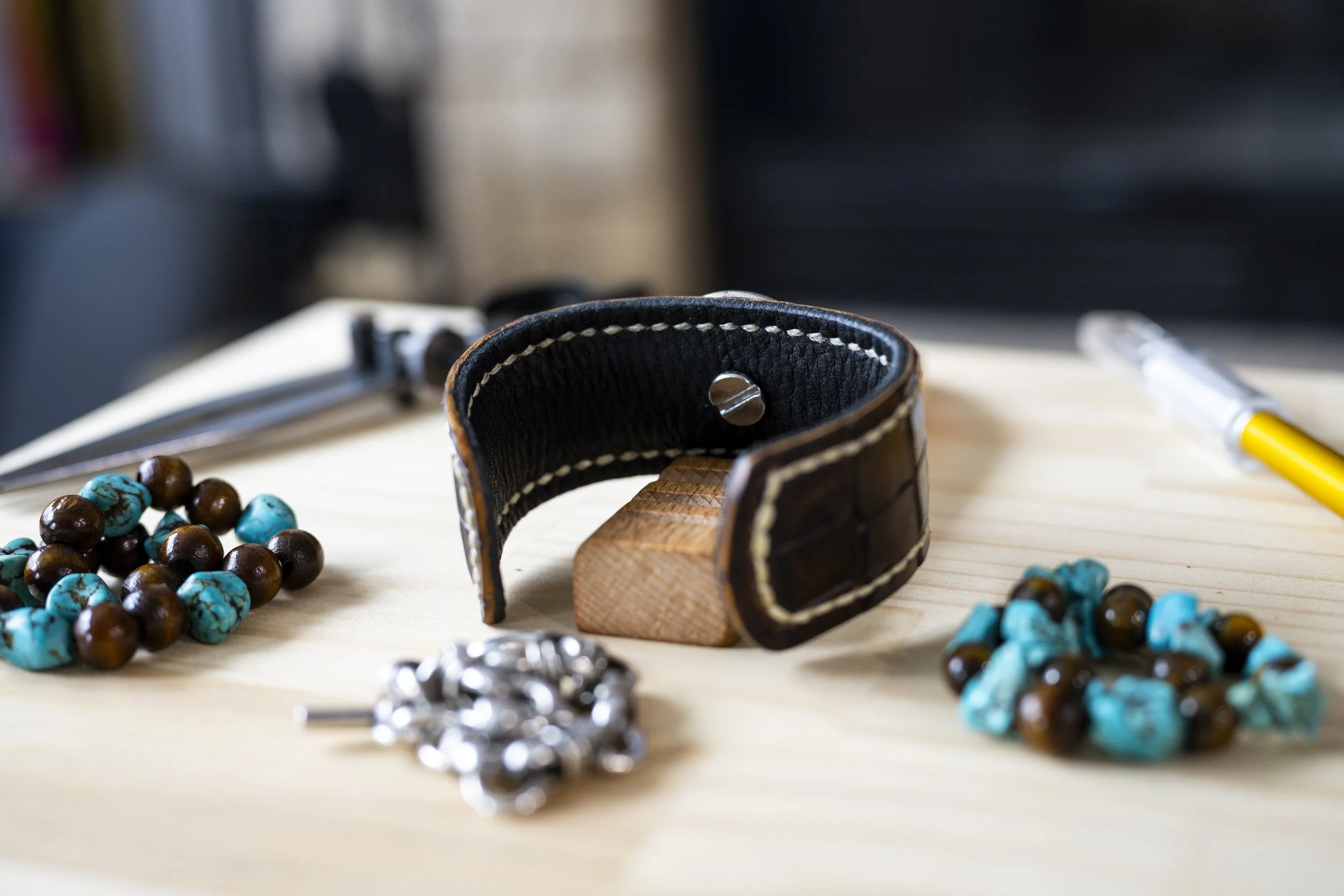 Close-up of a pet collar with beads, some bracelets and a pen on a light wooden surface, blurred background.