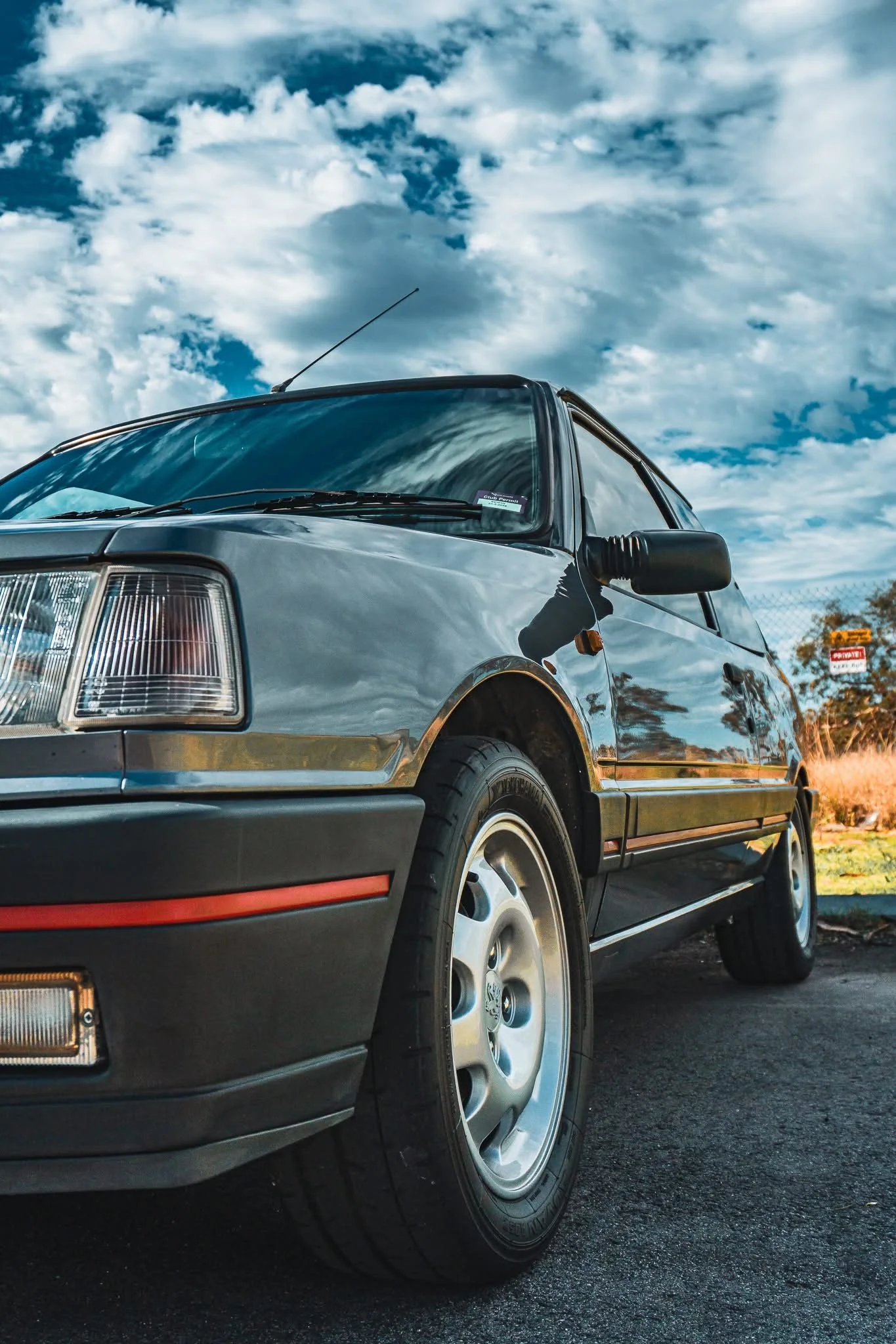 Close-up of the front side of a vintage black car parked outdoors, with cloudy sky in the background.