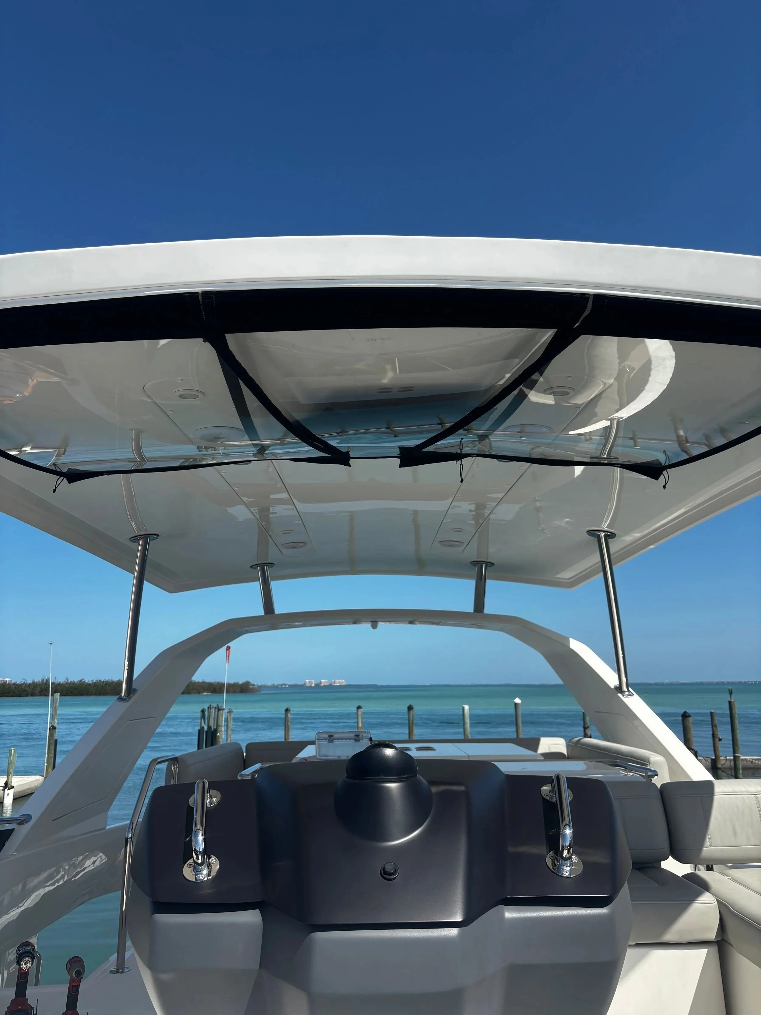 View from the cockpit of a yacht, showing the dashboard and steering wheel, with a skyline and water in the background under a clear blue sky.