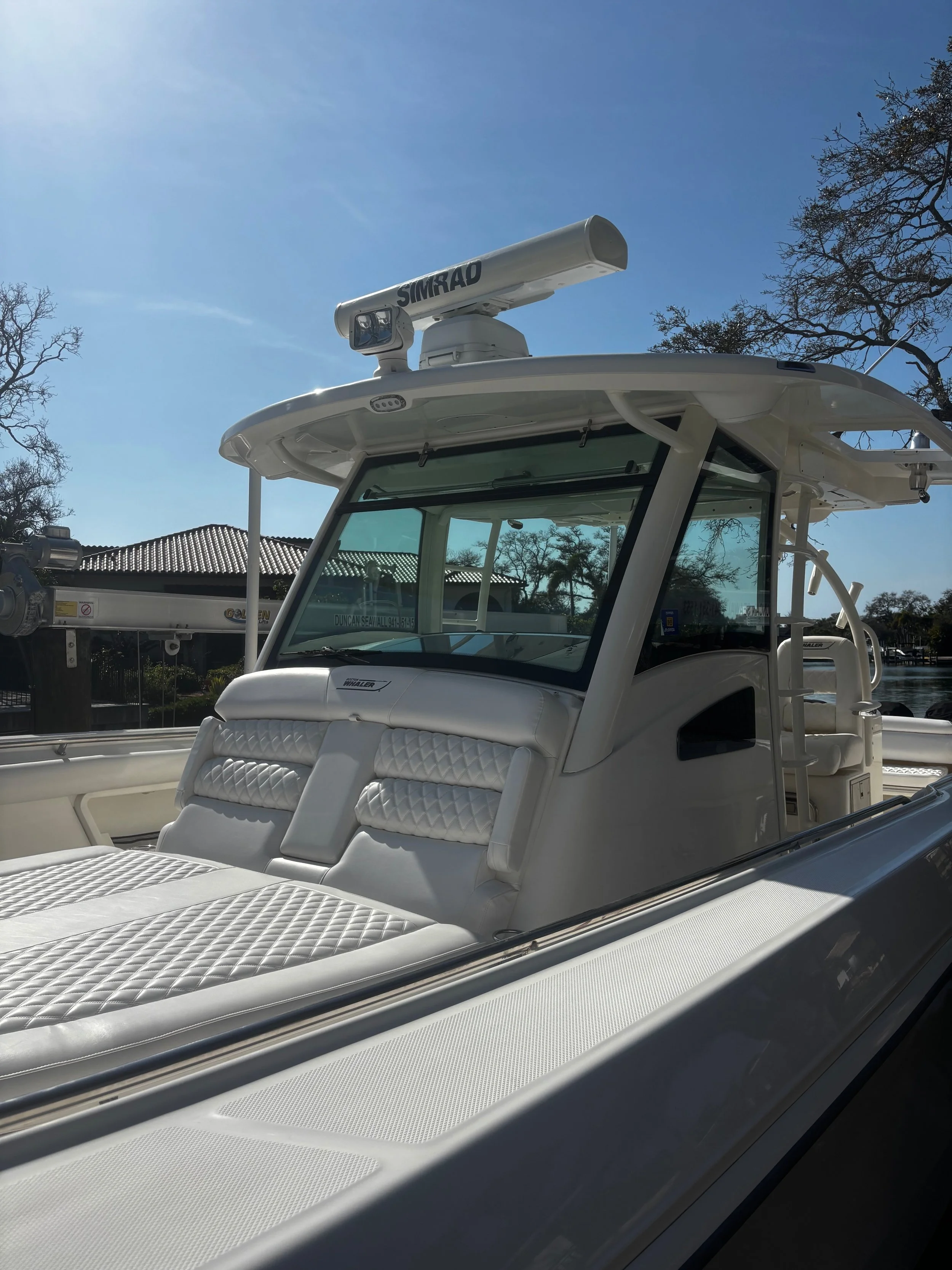 Close-up of the front seating area of a white boat, with cushioned sun pad seating and a radar mounted on top, under a clear blue sky.