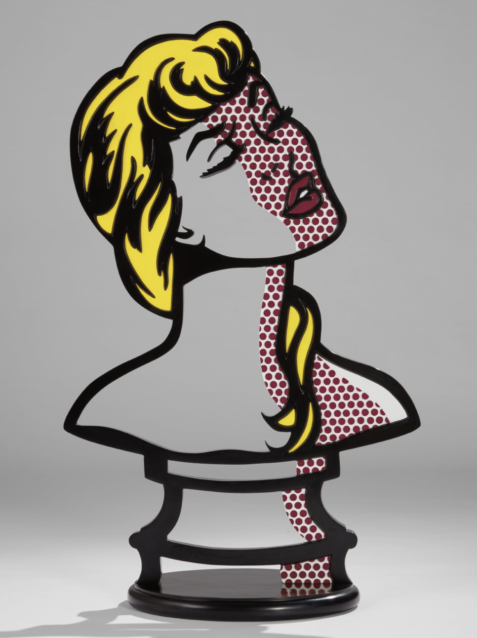 Roy Lichtenstein's iconic Sunlight Moonlight sculpture featuring a woman with blonde hair, with one half of her face and hair in yellow and black, and the other half in red with a polka dot pattern, on a round black base.