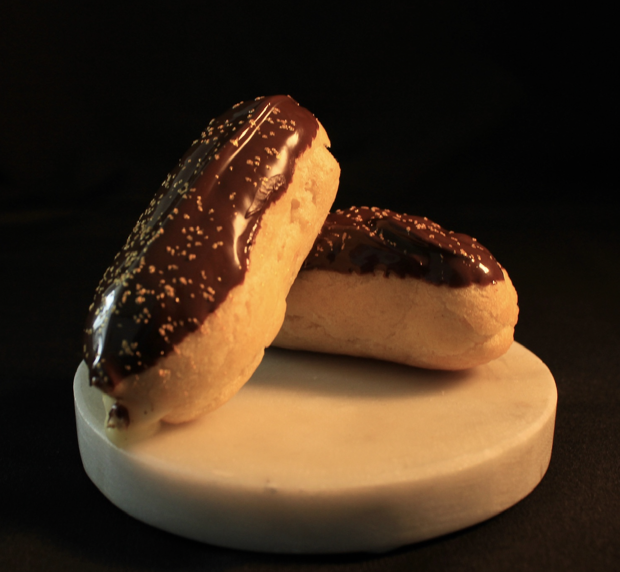 Two cookies topped with chocolate glaze and sprinkles on a white plate against black background.