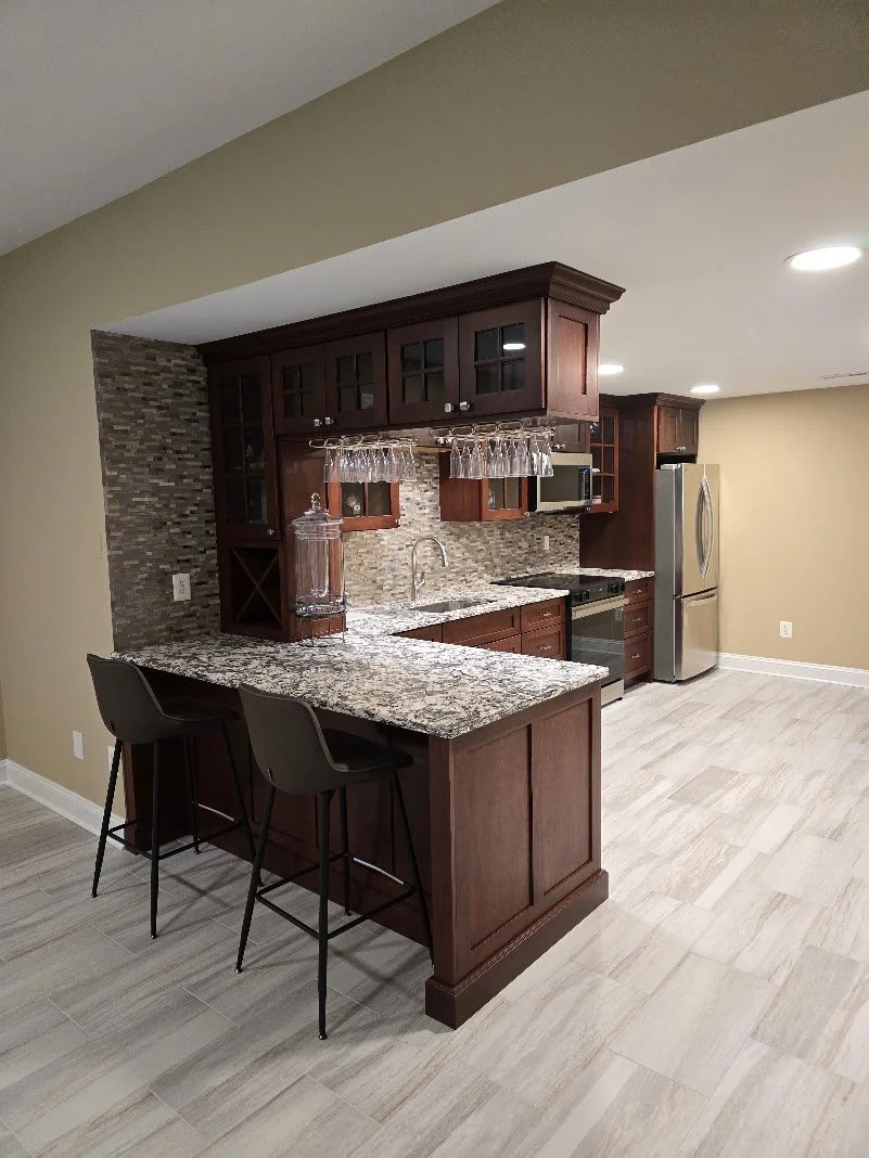 Kitchen with dark wood cabinets, granite countertops, tile backsplash, stainless steel refrigerator, and two bar stools at the counter.
