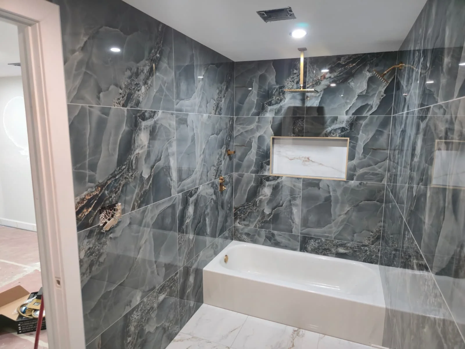 Bathroom under construction featuring dark gray marble tile walls, a white bathtub, and a built-in marble niche. Shower fixtures are not yet installed.