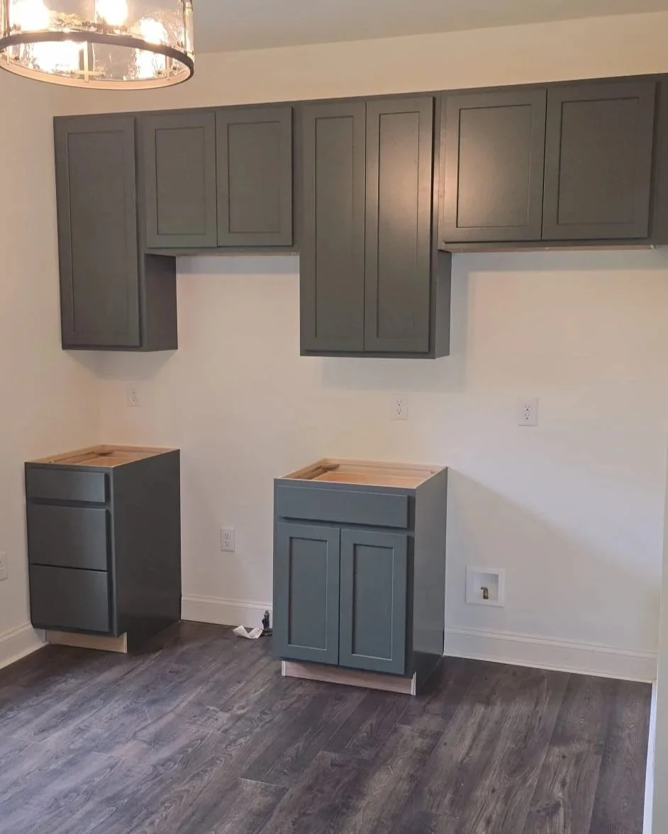 Kitchen with gray cabinets, with some cabinets unfinished and missing doors, and a dark wood floor.
