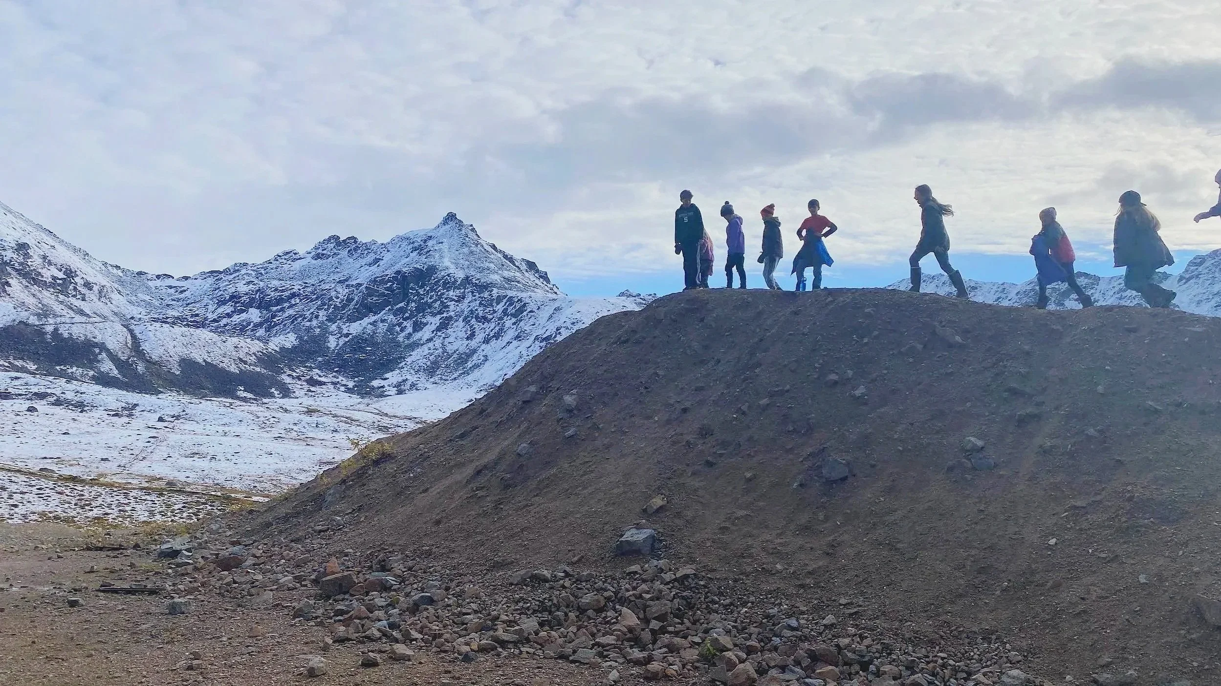 Group of people hiking on a mountain trail with snow-capped peaks in the background.