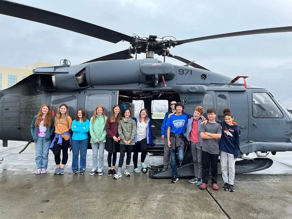Group of children standing in front of a military helicopter outdoors.