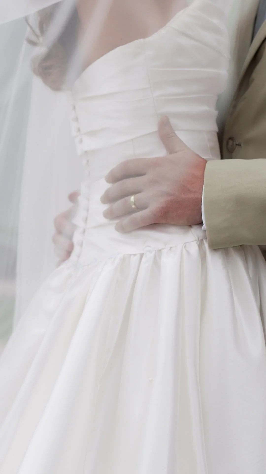 Close-up of a person in a white clothing, gloves, and an off-white jacket, with their hand resting on their waist.