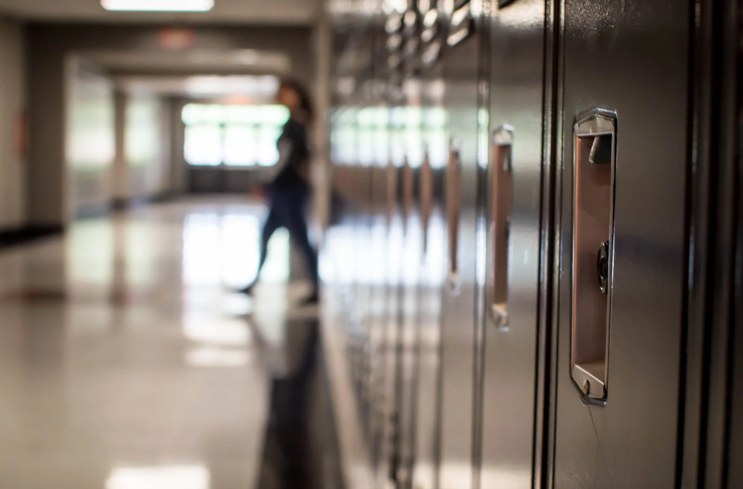 Close-up of school lockers with a blurred background of a hallway with a person walking.