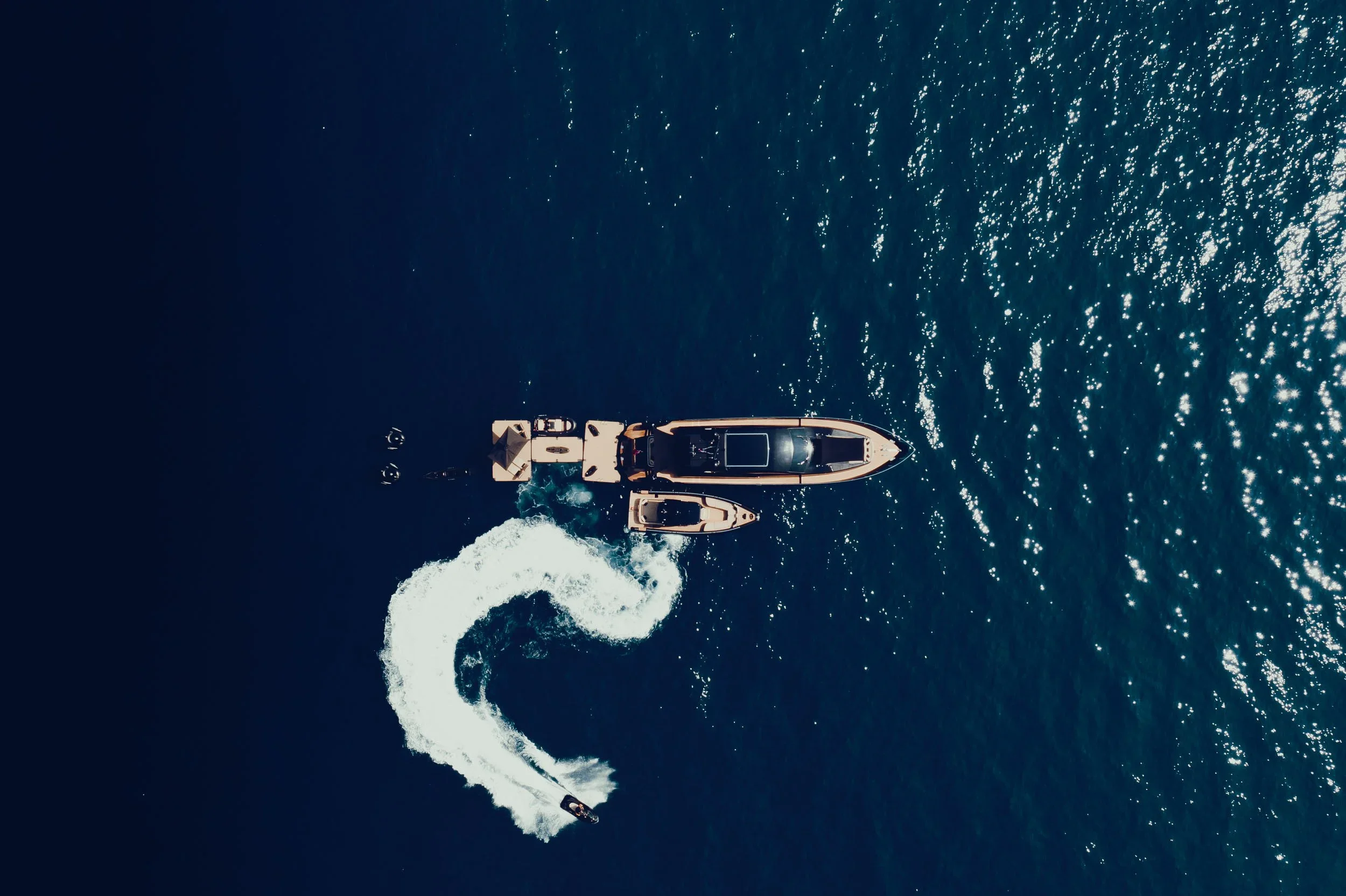 Aerial view of a motorboat cruising through dark blue water, creating a white wake with sparkling reflections on the surface.