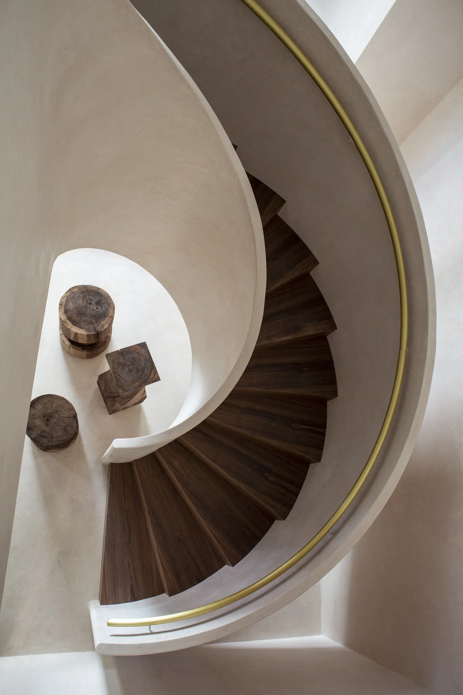 View of a spiral staircase with wooden steps, a white curved railing, and a gold-colored handrail, photographed from above.