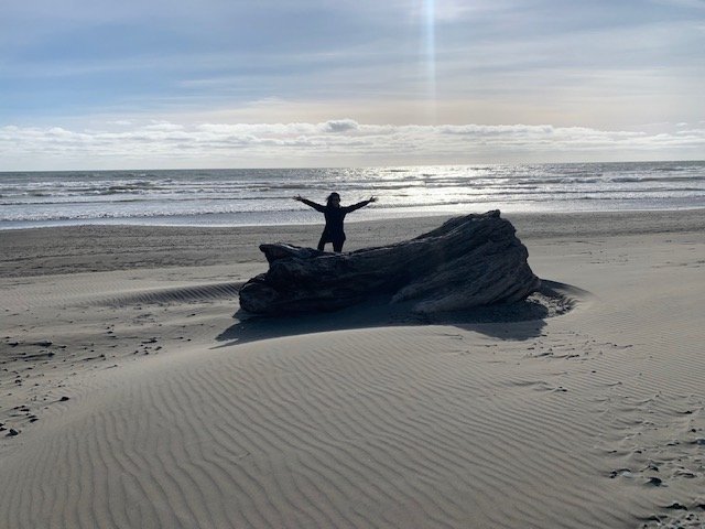 Shai standing atop a large piece of driftwood on an uninhabited Washington State beach.