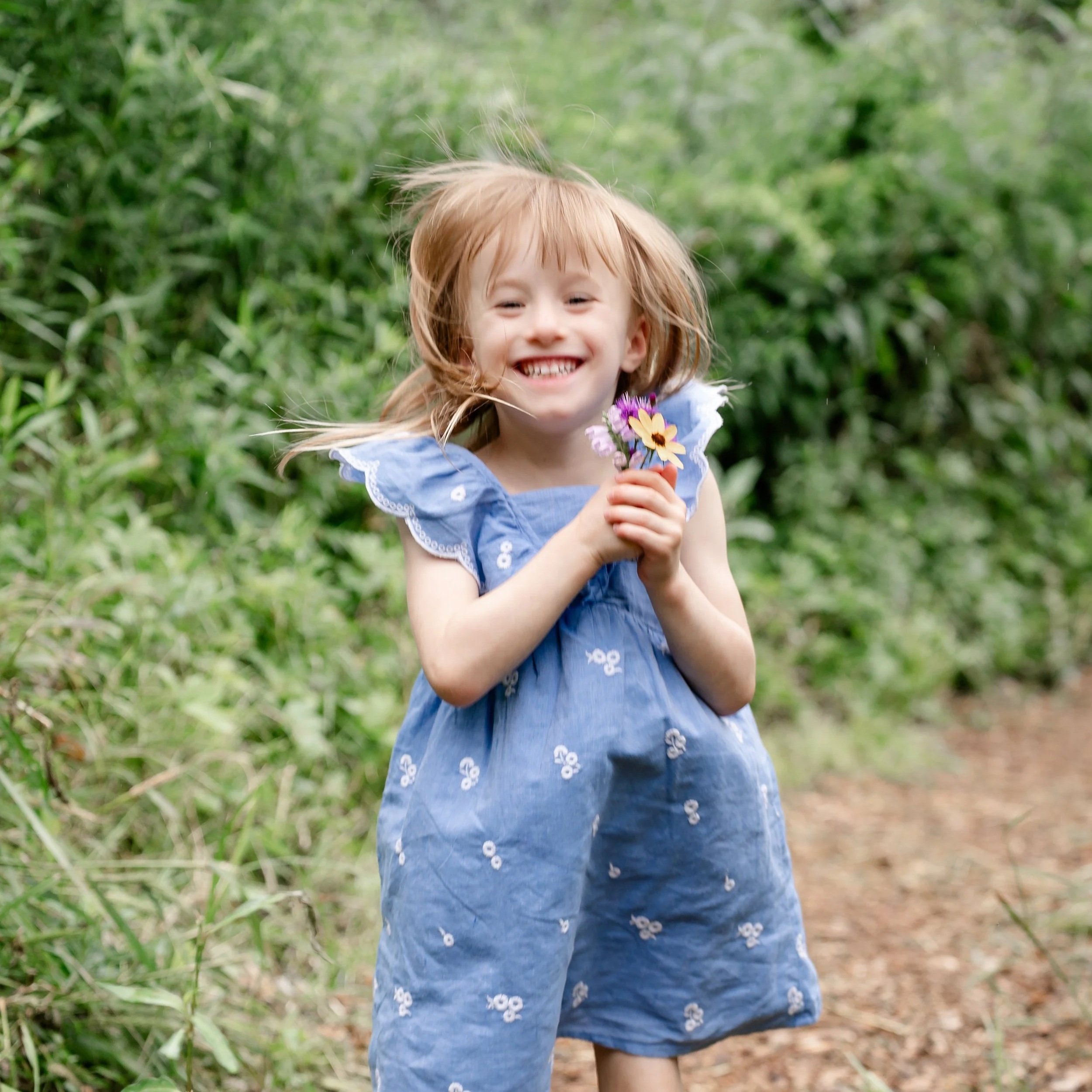 A young girl with red hair smiling and holding a small bouquet of colorful flowers outdoors in a green, leafy environment located in Glenview IL.