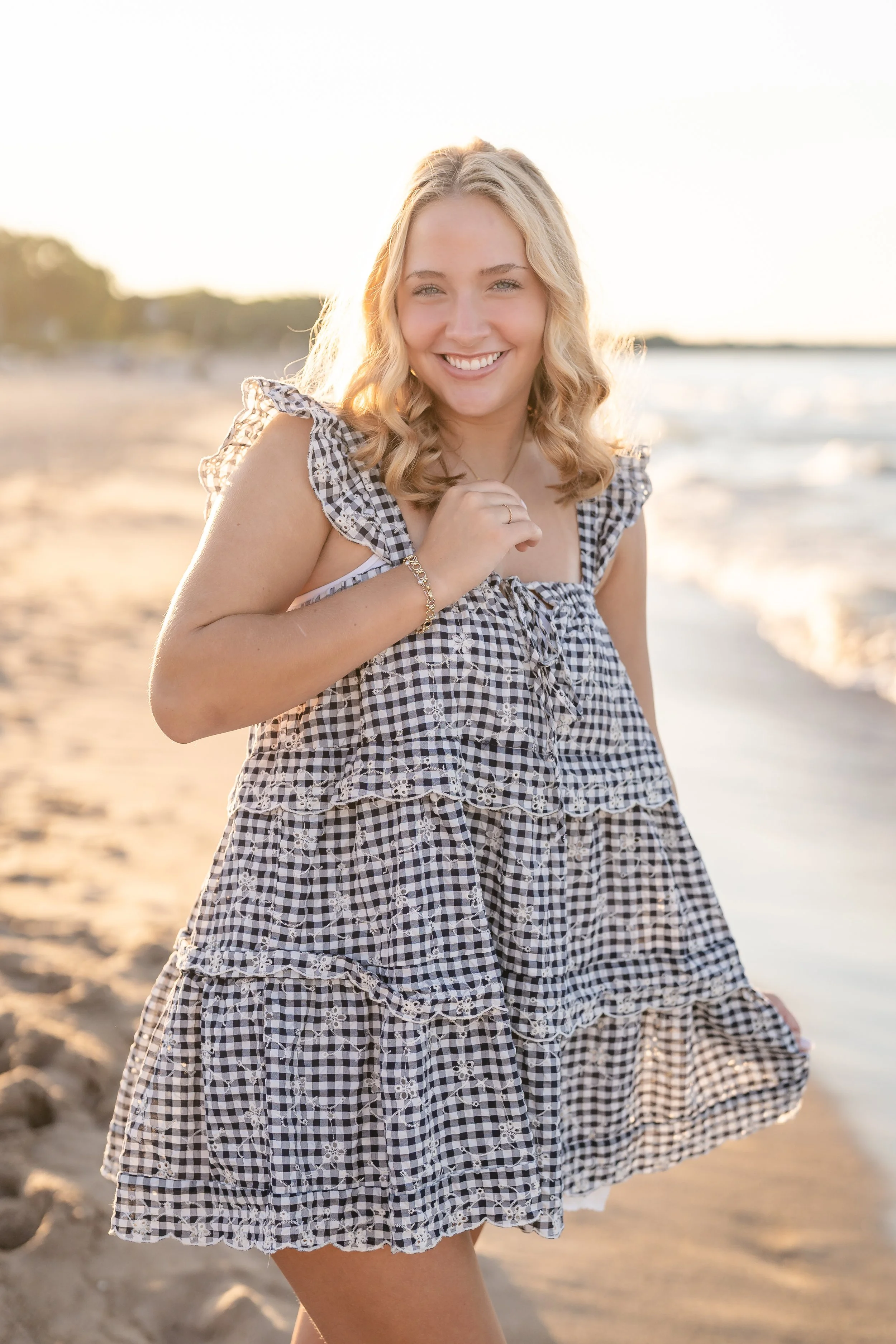 Young woman smiling at the beach wearing a black and white gingham dress during sunset, located in Wilmette at Gillson Beach.