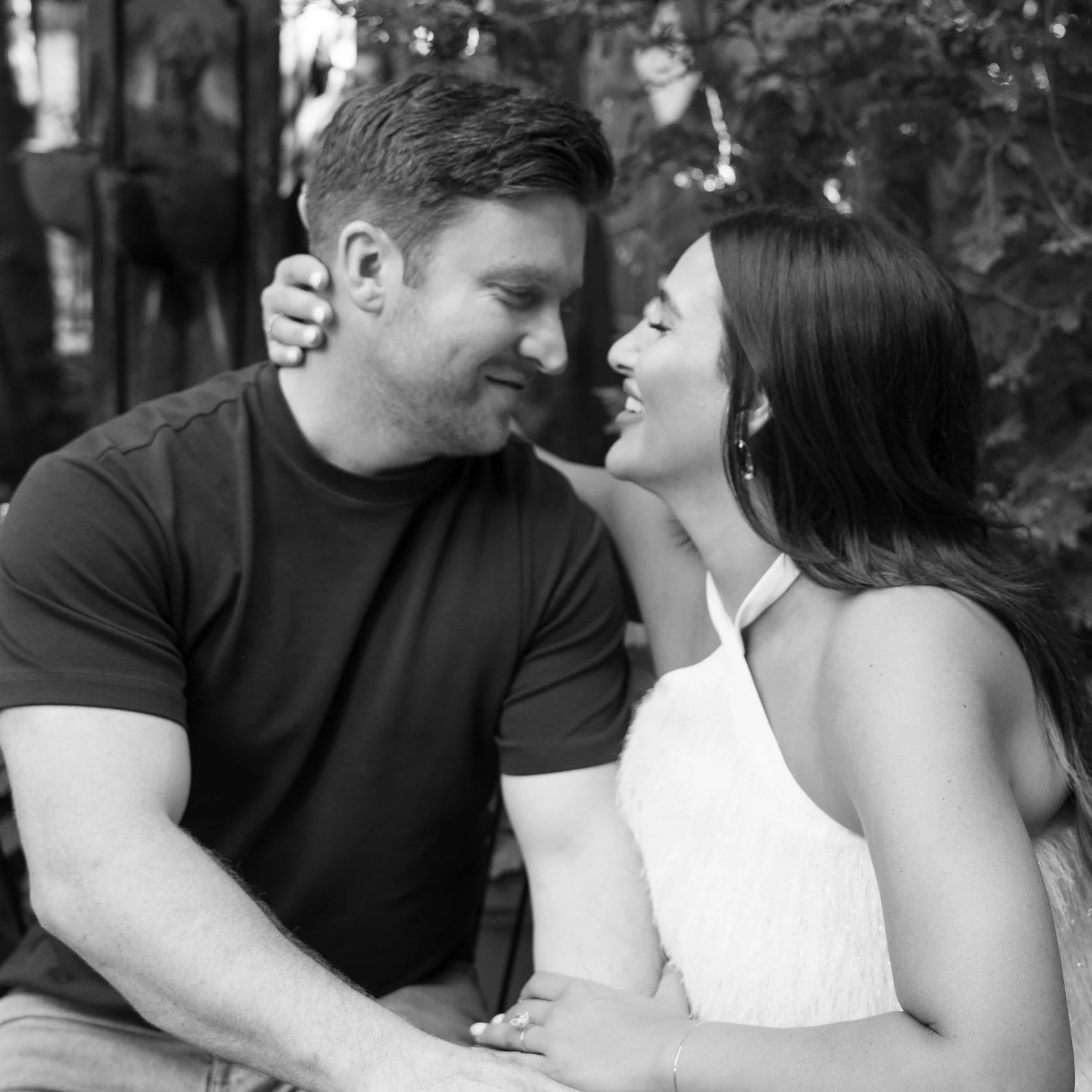 A black and white photo of an engaged couple close together, smiling and leaning their foreheads against each other, in an outdoor setting with trees in the background planning their wedding in Chicago, IL.