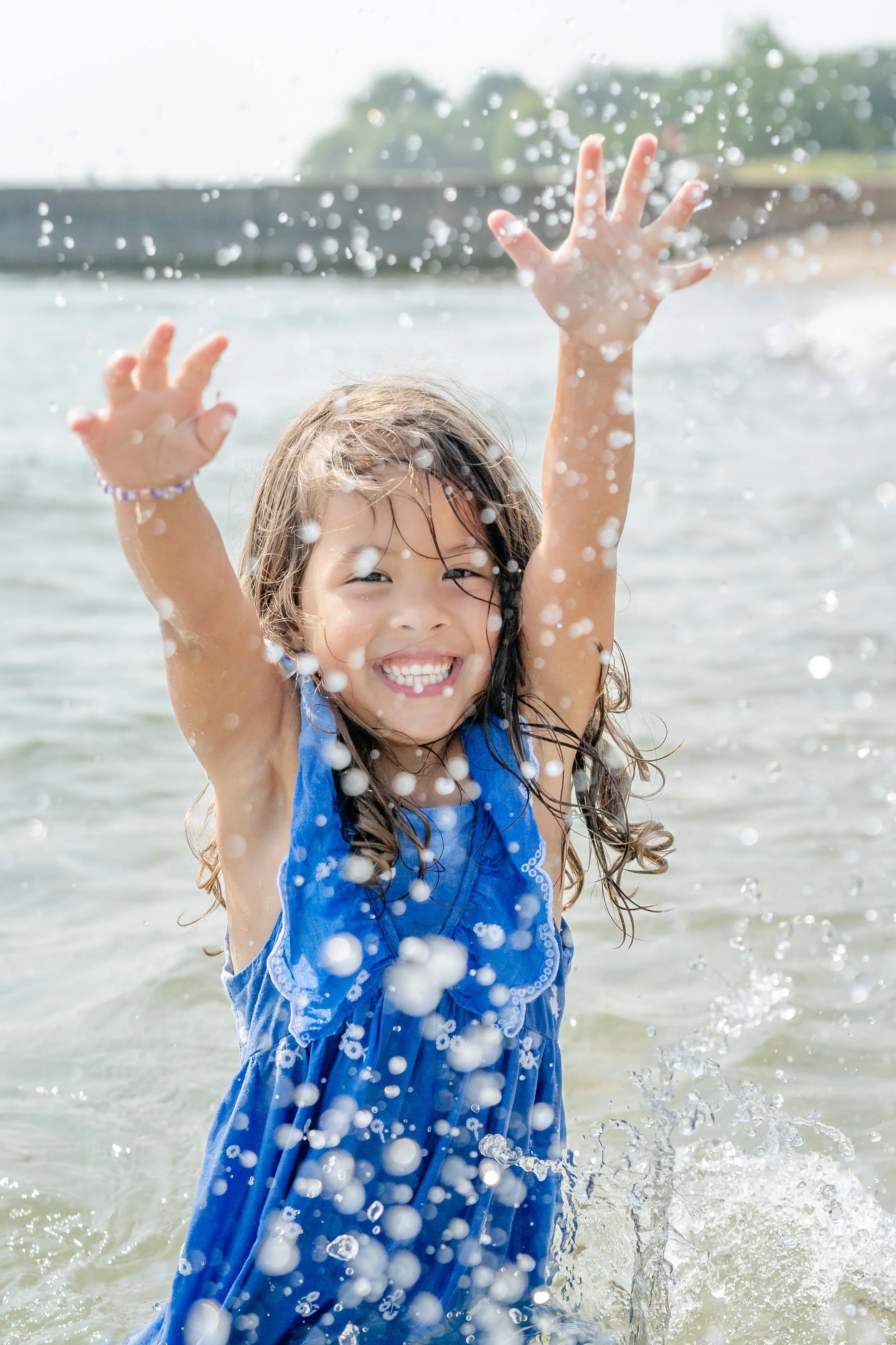 Girl in a blue dress splashing and laughing in the water in Wilmette, IL