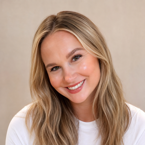 Close-up of a smiling woman with long blonde hair, wearing a white shirt, against a neutral background.