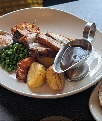 Roast beef with potatoes, green peas, yorkshire pudding, and gravy on a white plate.