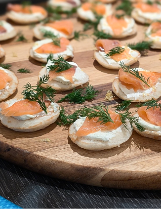 Cream cheese bagel bites topped with smoked salmon and fresh dill, arranged on a wooden cutting board.