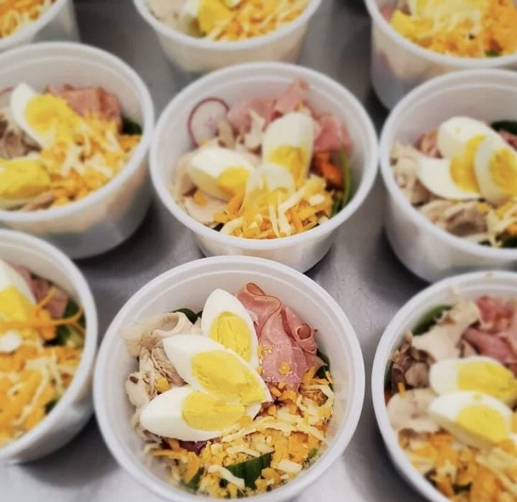 Close-up of small bowls filled with salad, sliced boiled eggs, shredded cheese, ham, and vegetables.
