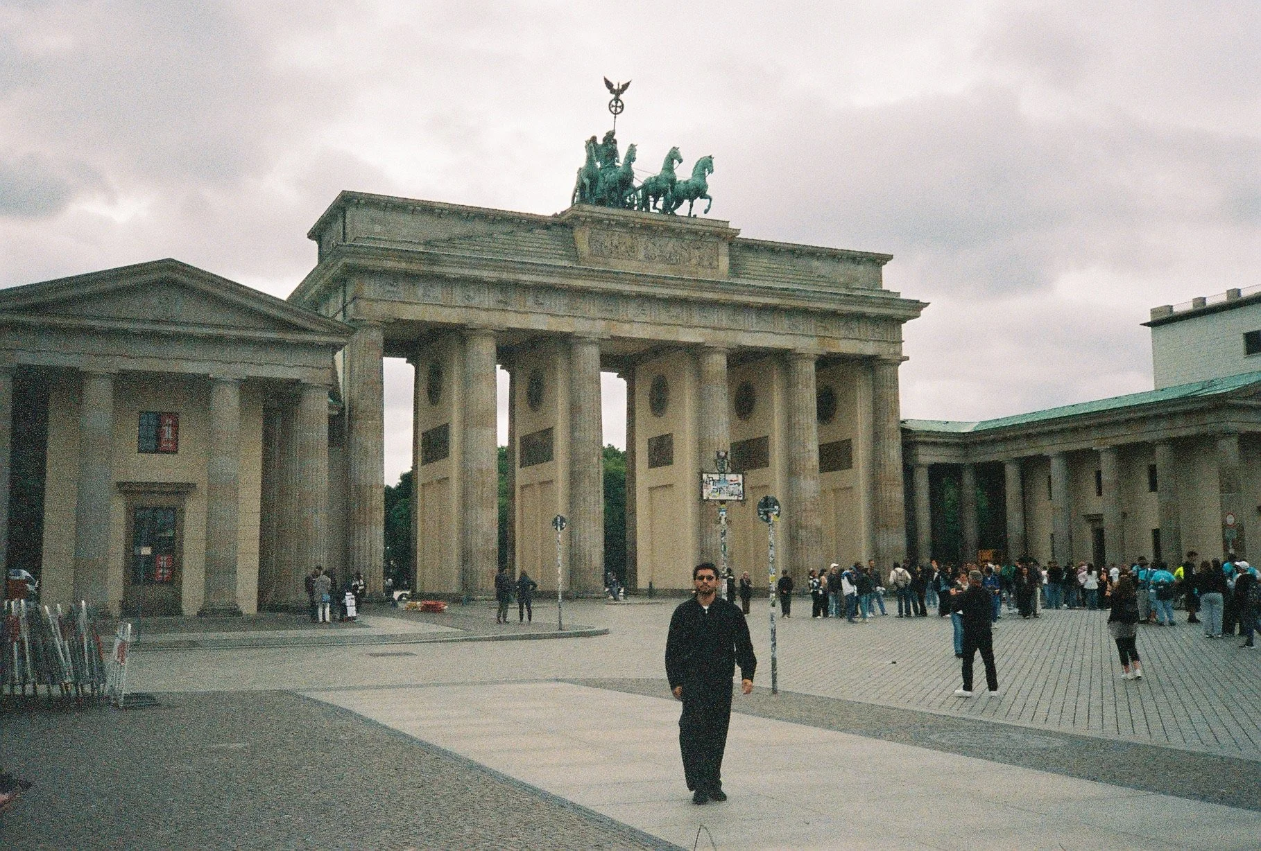 The Brandenburg Gate in Berlin, Germany, with people walking and standing in front of it on a cloudy day.