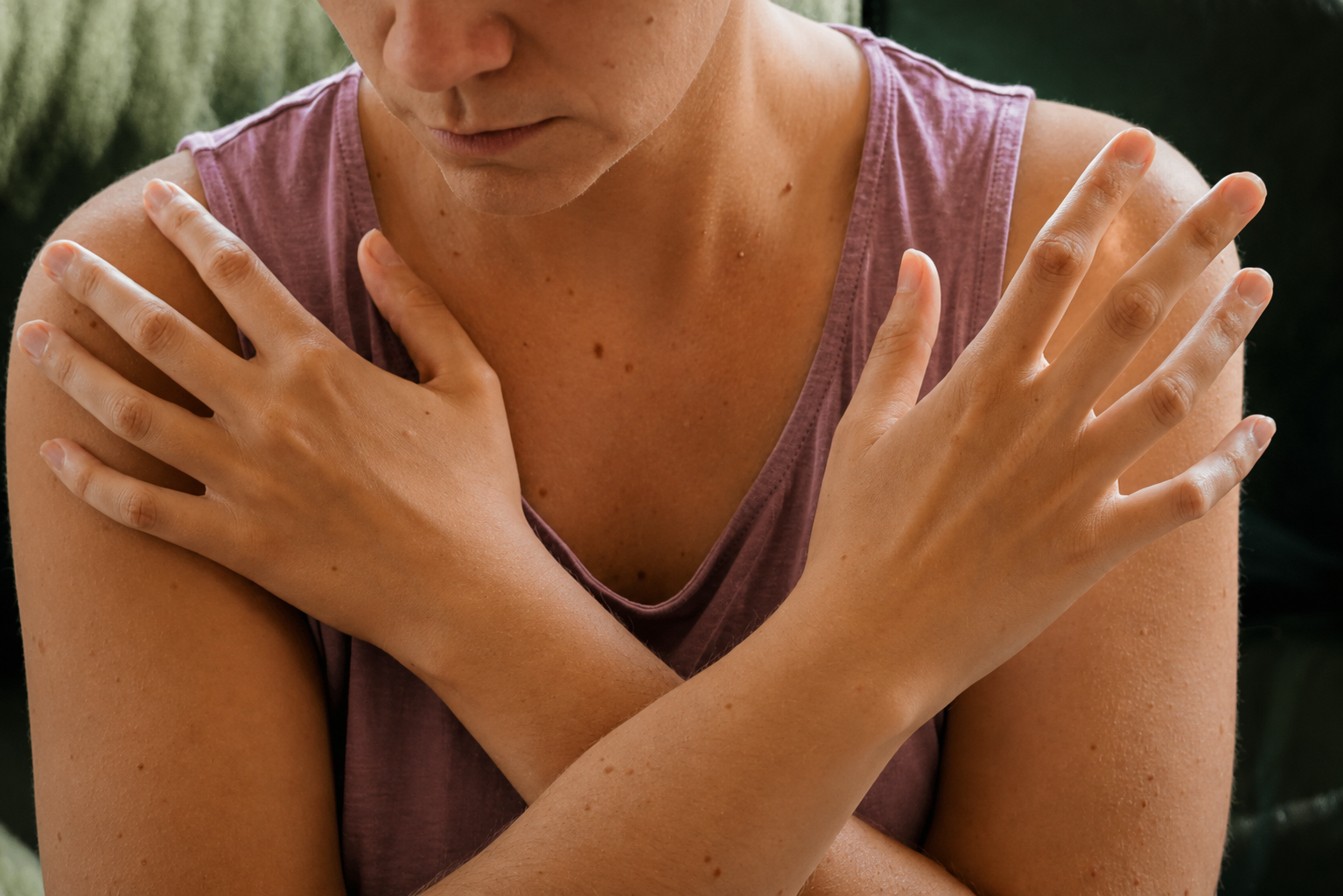 A person with their arms crossed over their chest, wearing a pink sleeveless top, with various moles or blemishes on their skin.