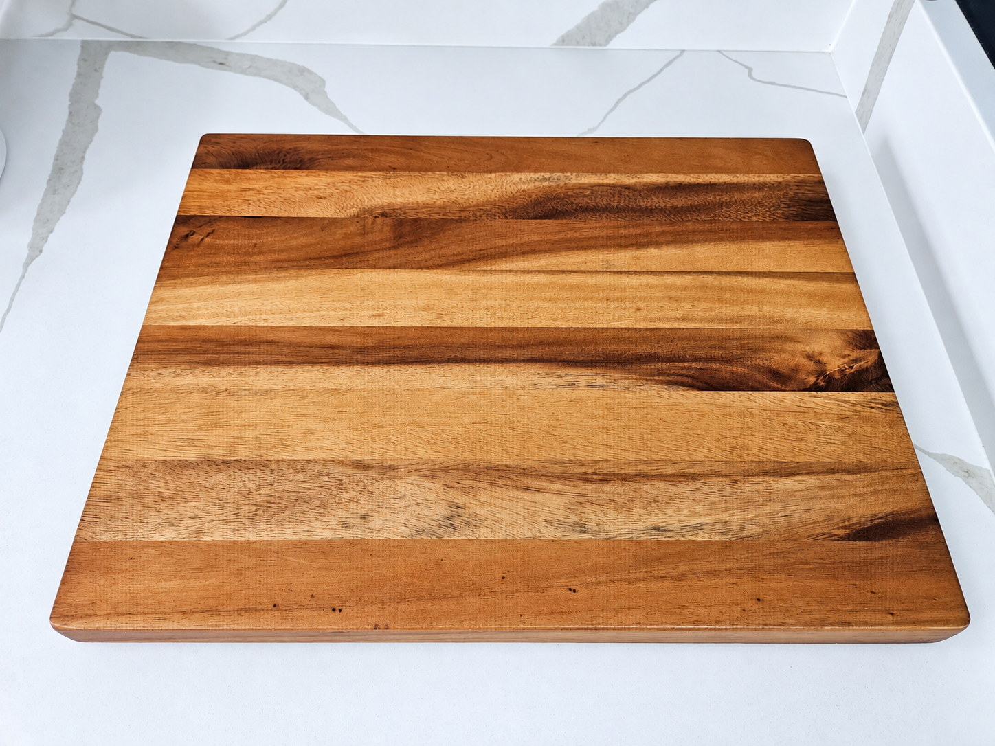 Large striped hardwood cutting board with warm natural wood grain resting on a white marble countertop