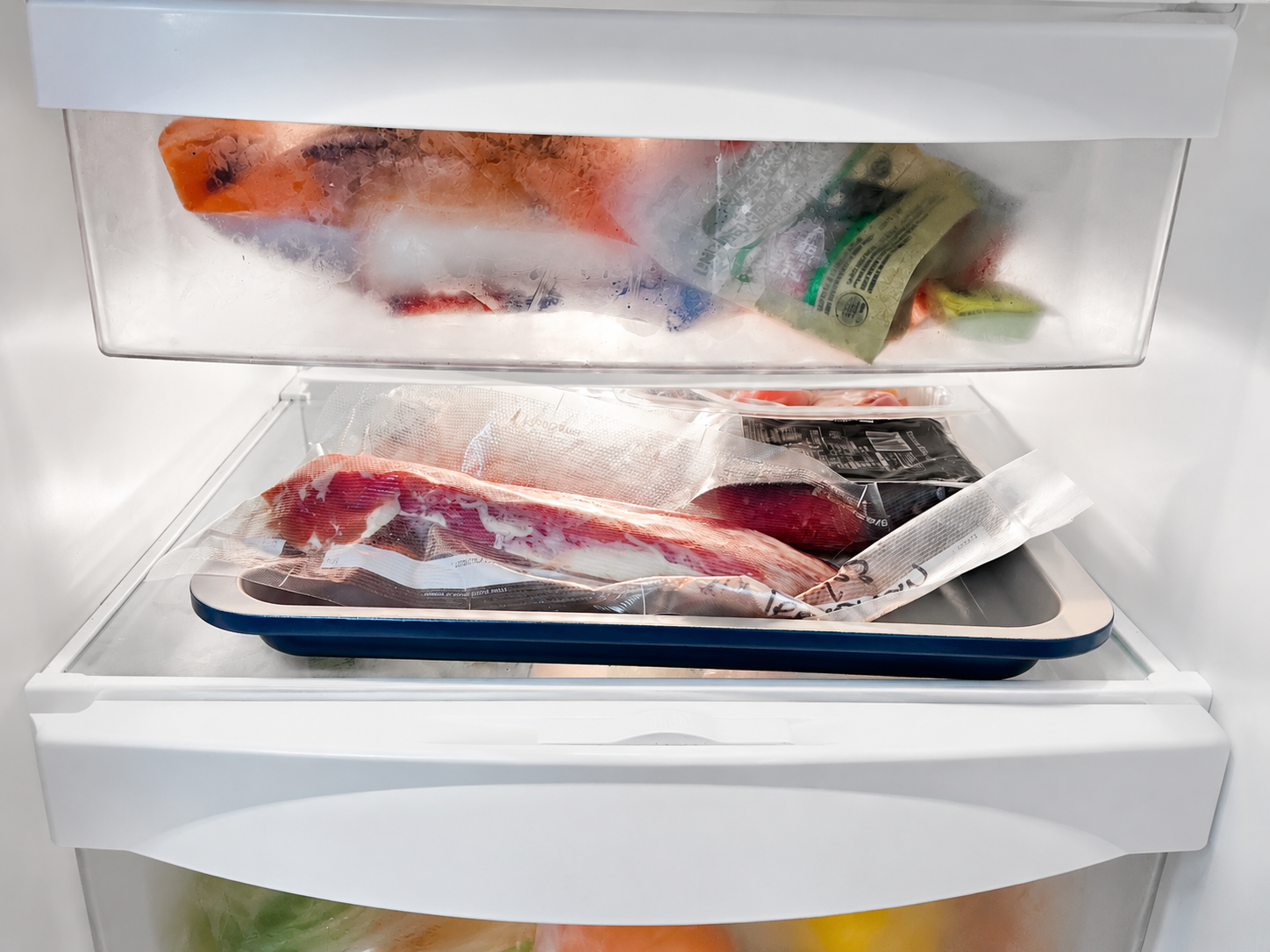 Vacuum-sealed raw meat stored on a tray on the bottom shelf of a refrigerator for safe thawing.